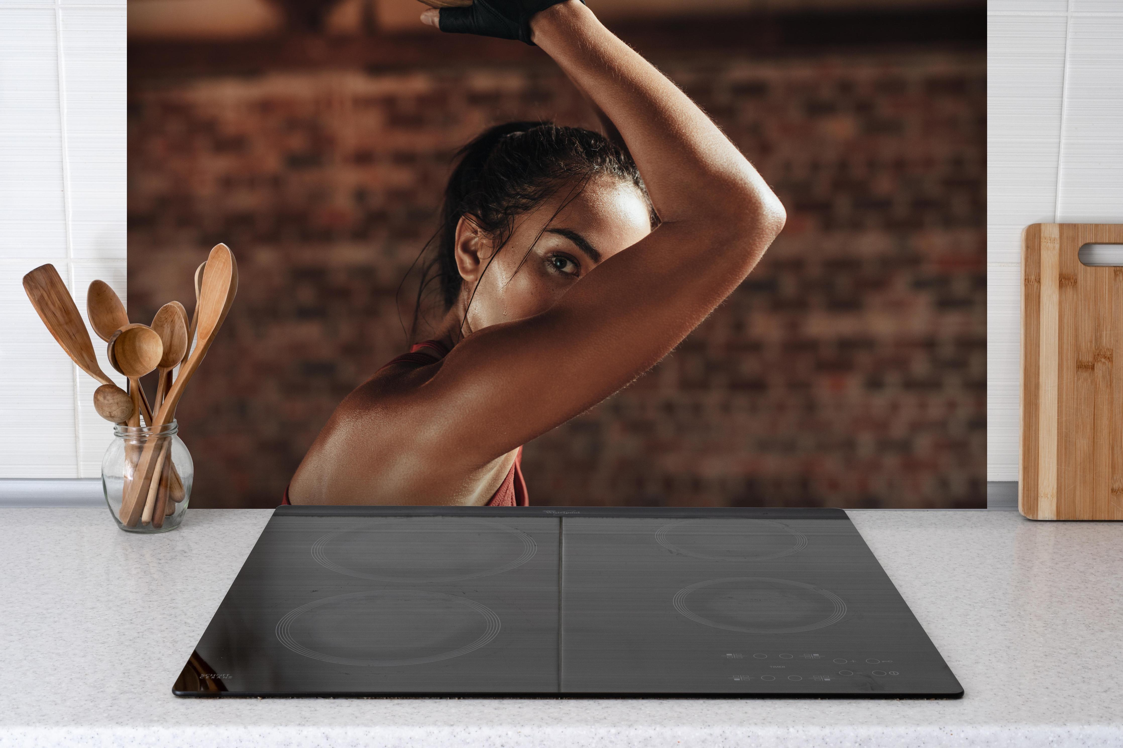 Spritzschutz - Starke Frau beim Training mit Dip-Ringen hinter einem Cerankochfeld zwischen Holz-Kochutensilien