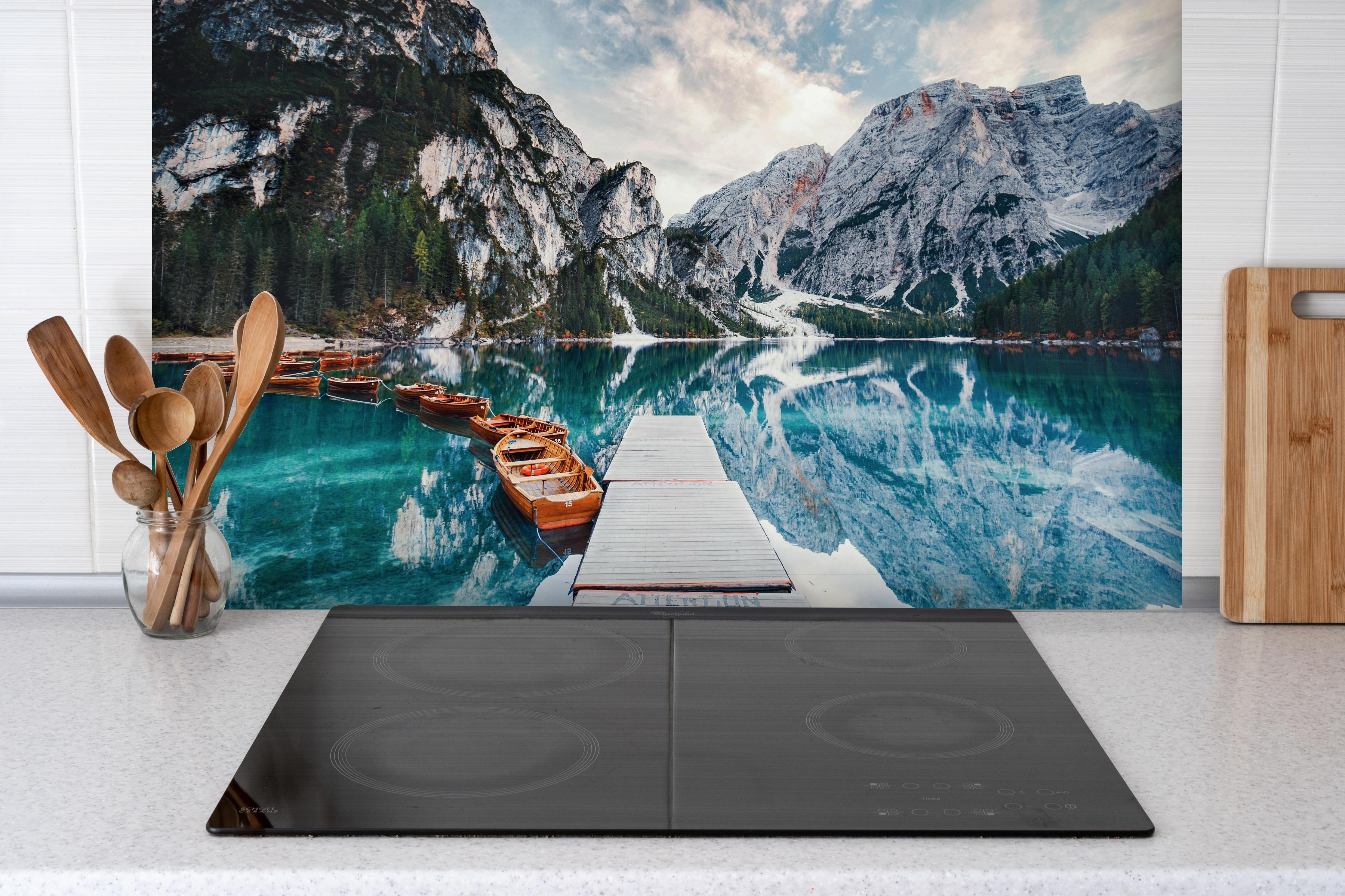 Spritzschutz - Steg am Bergsee mit Booten hinter einem Cerankochfeld zwischen Holz-Kochutensilien