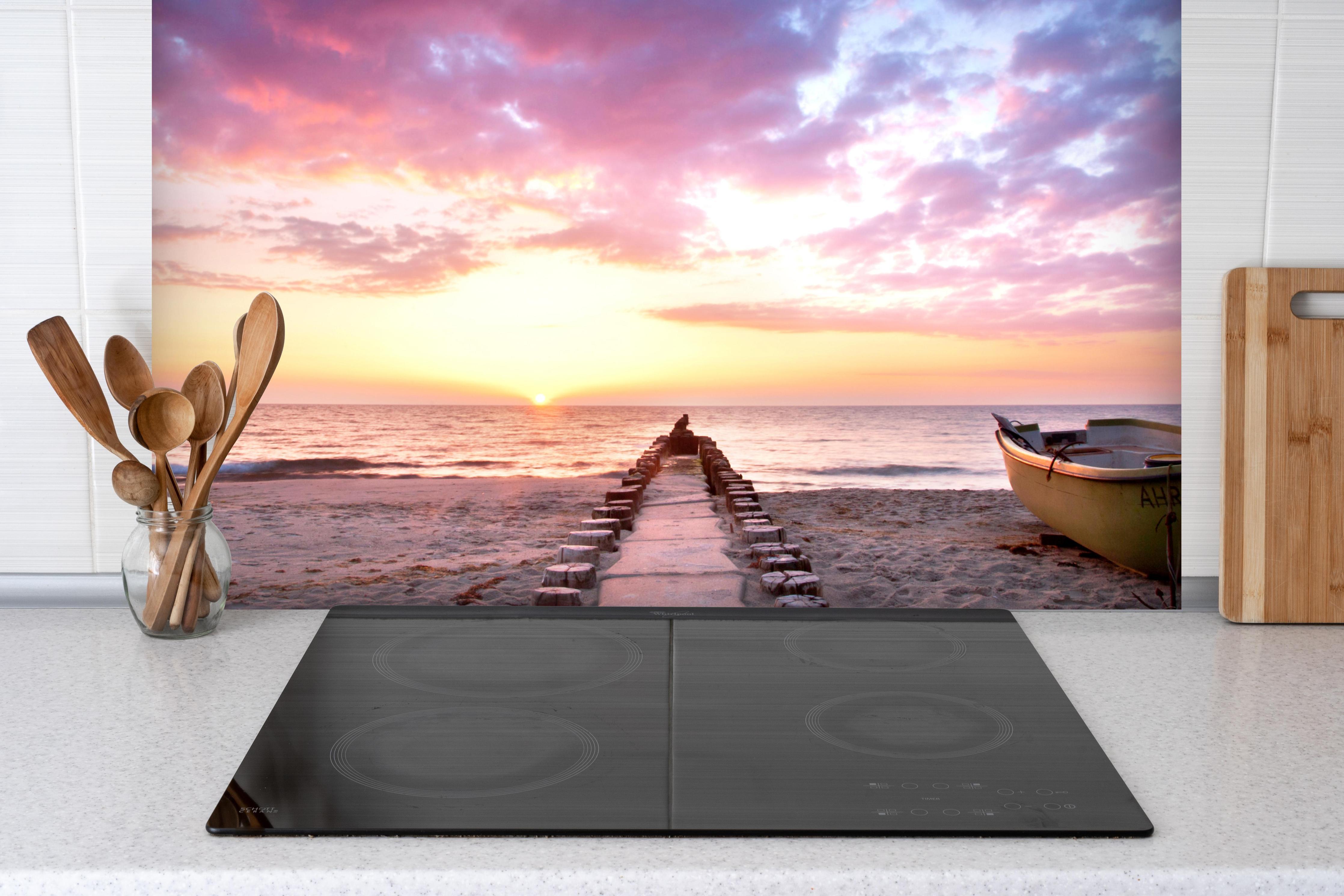 Spritzschutz - Steg ins Meer bei Abendsonne hinter einem Cerankochfeld zwischen Holz-Kochutensilien