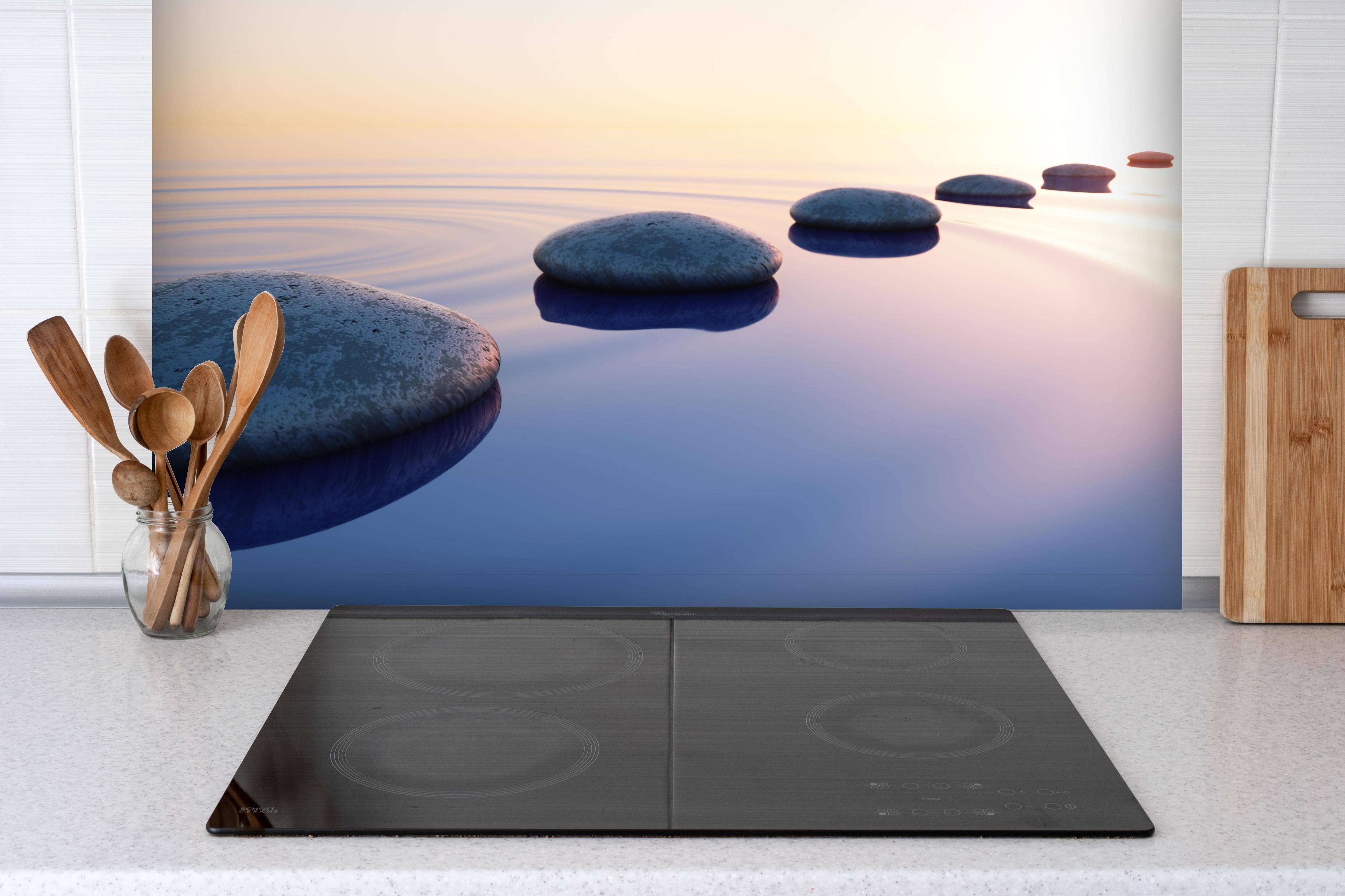 Spritzschutz - Steine im See bei Sonnenaufgang hinter einem Cerankochfeld zwischen Holz-Kochutensilien