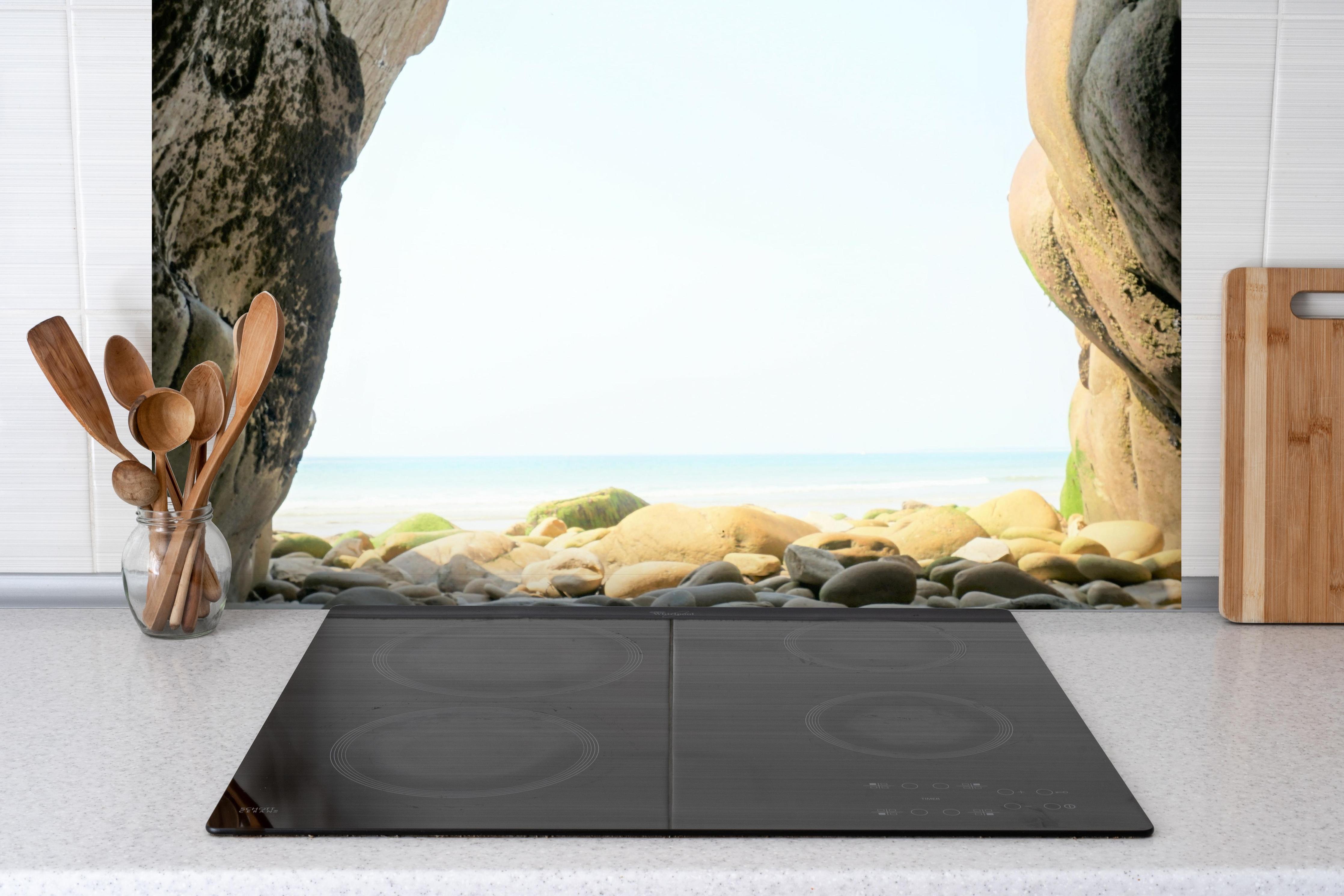 Spritzschutz - Steinstrand zwischen Felsen an Küste hinter einem Cerankochfeld zwischen Holz-Kochutensilien