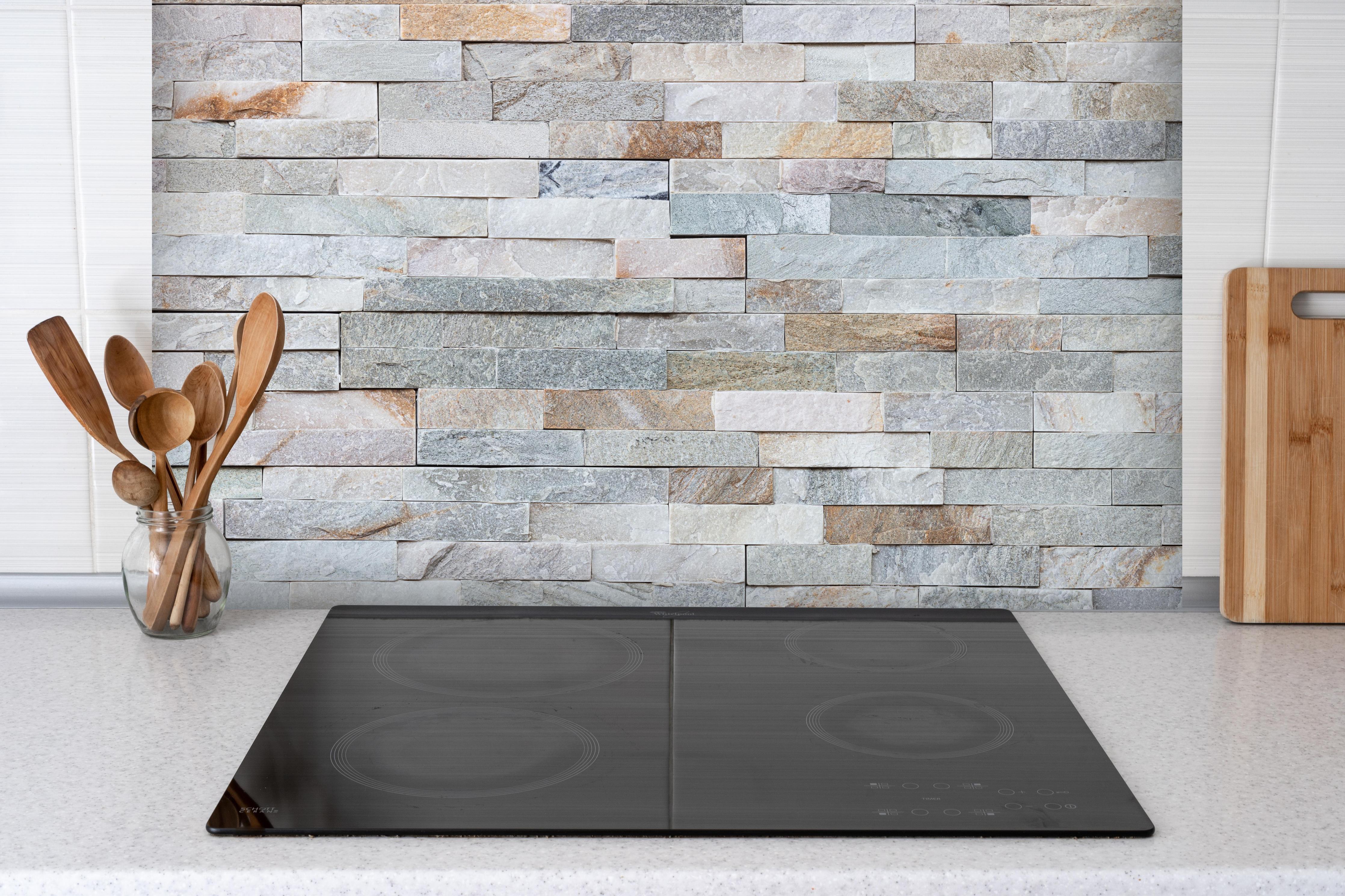 Spritzschutz - Steinwandmuster hinter einem Cerankochfeld zwischen Holz-Kochutensilien