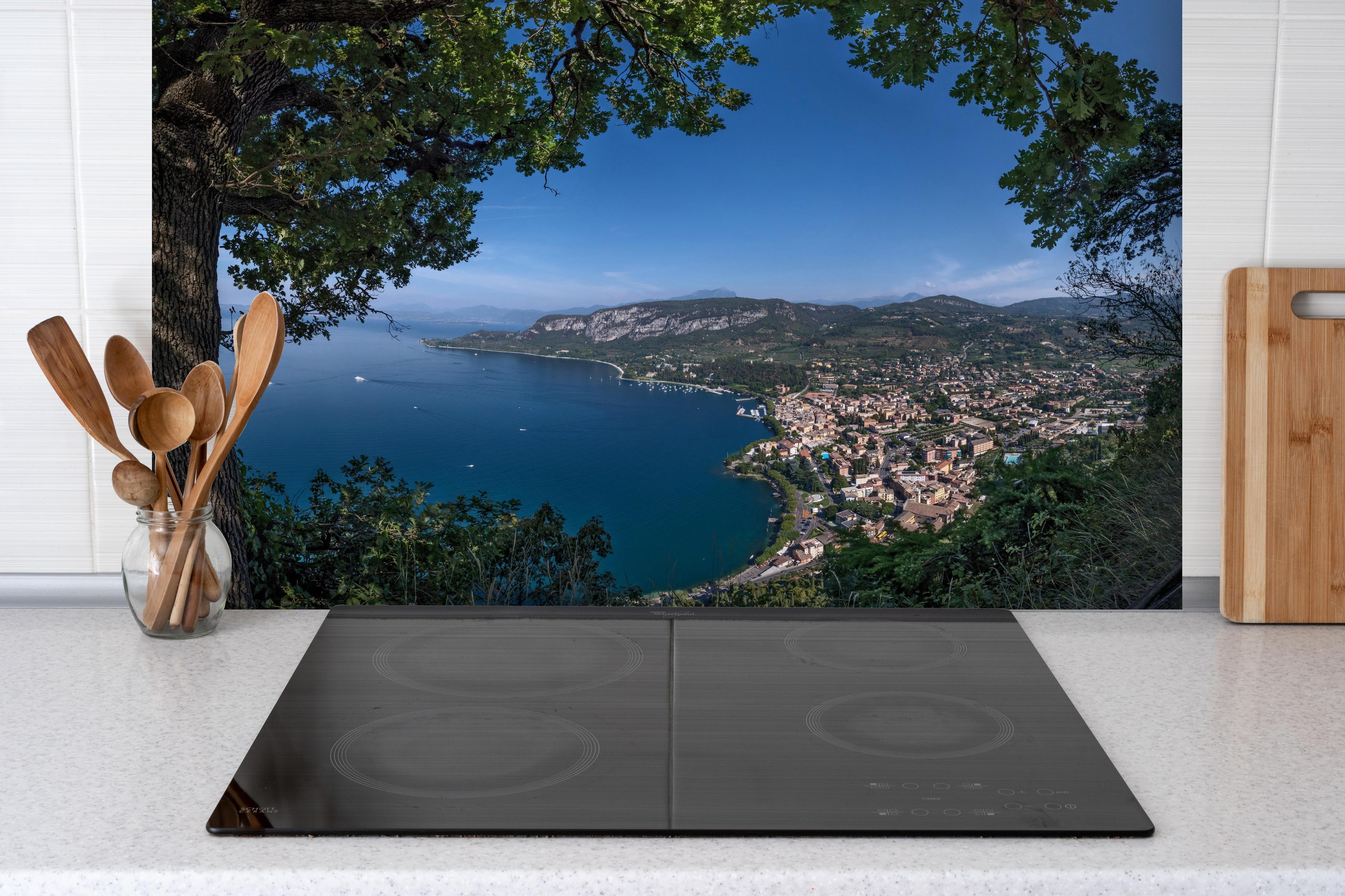 Spritzschutz - Traumhafter Ausblick auf Gardasee Italien hinter einem Cerankochfeld zwischen Holz-Kochutensilien