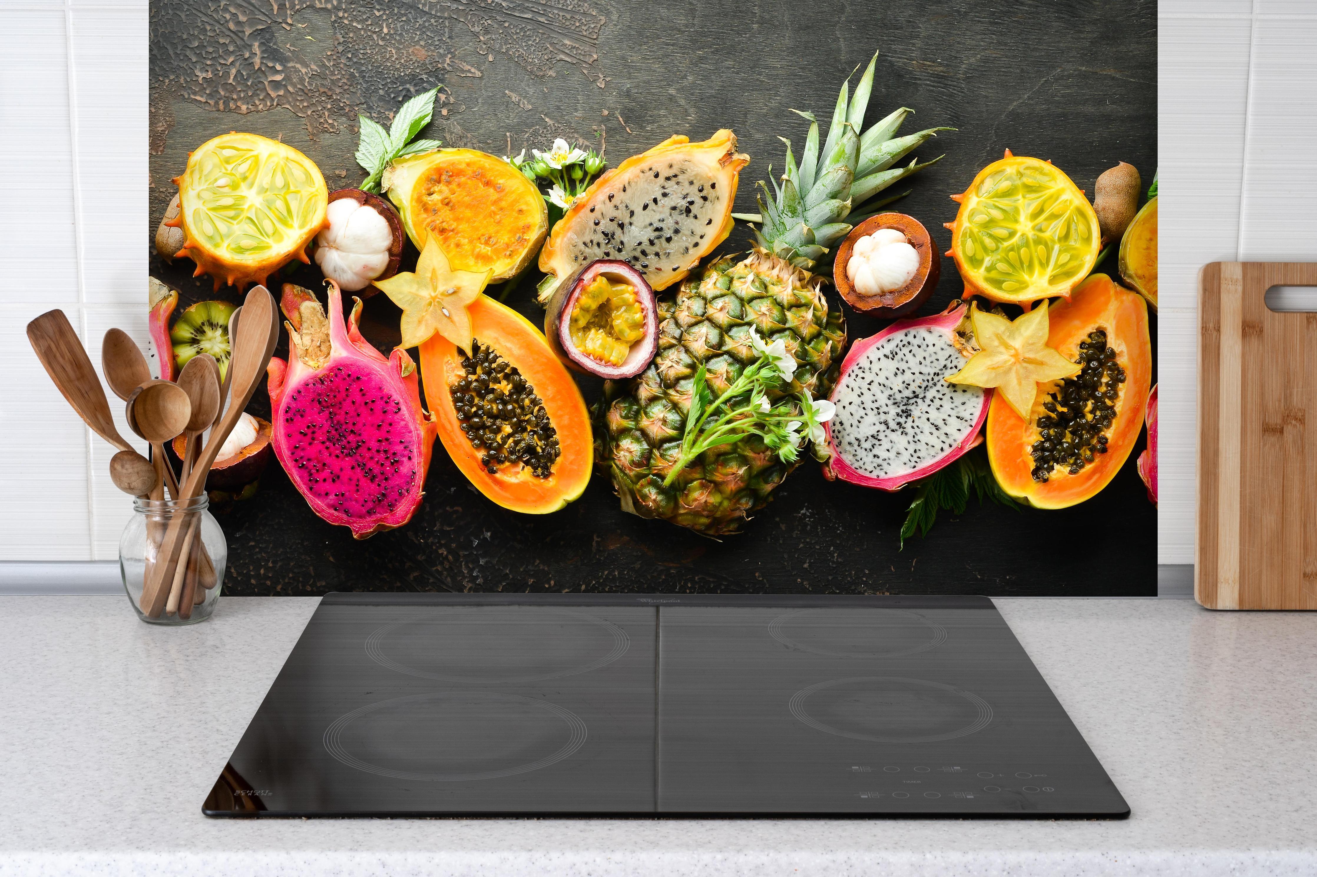 Spritzschutz - Tropische Früchte hinter einem Cerankochfeld zwischen Holz-Kochutensilien