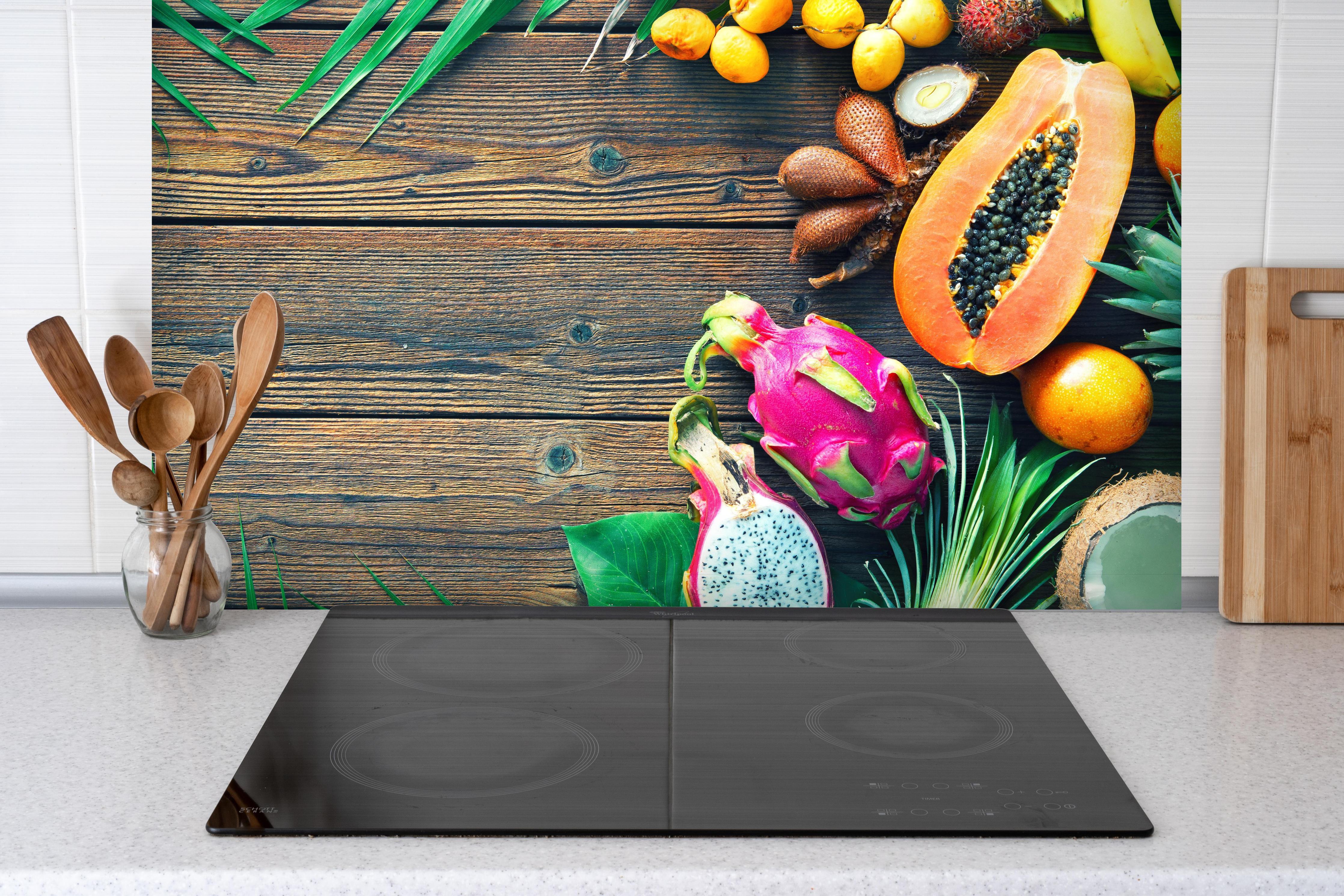 Spritzschutz - Tropische Früchte auf Holztisch hinter einem Cerankochfeld zwischen Holz-Kochutensilien