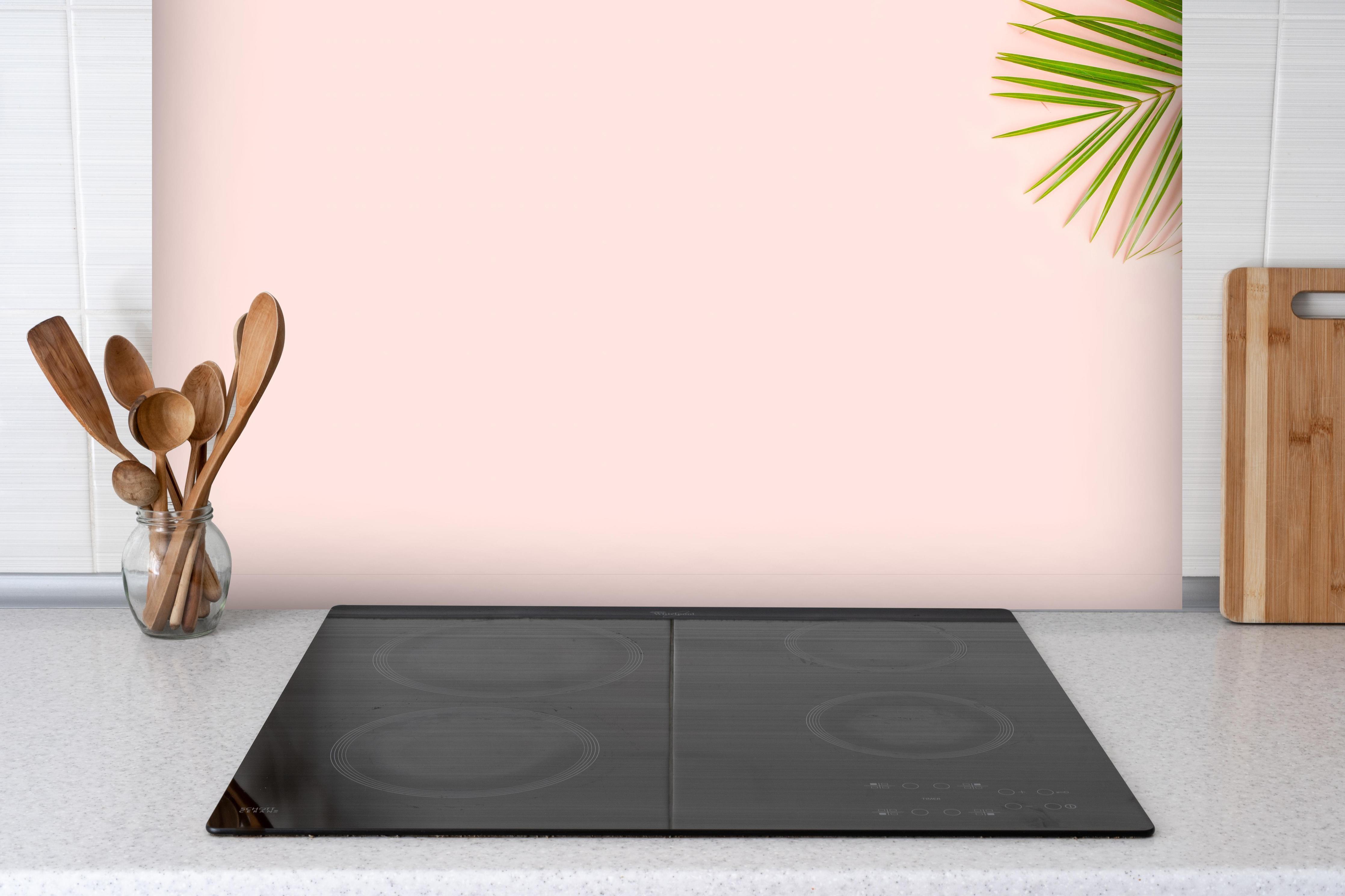 Spritzschutz - Tropische Palmenblätter mit Strohhut hinter einem Cerankochfeld zwischen Holz-Kochutensilien