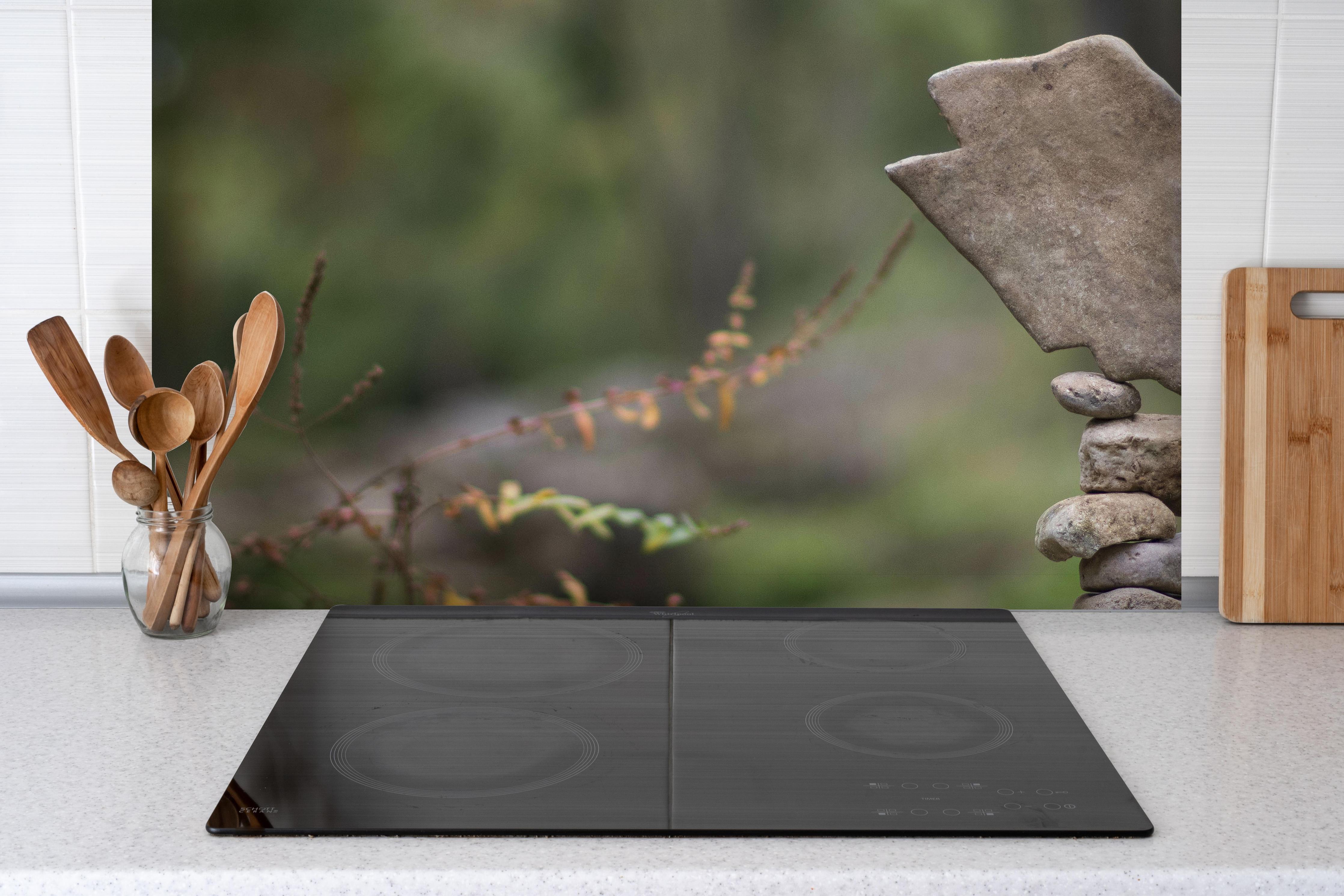 Spritzschutz - Turm aus Steinen im Wald hinter einem Cerankochfeld zwischen Holz-Kochutensilien