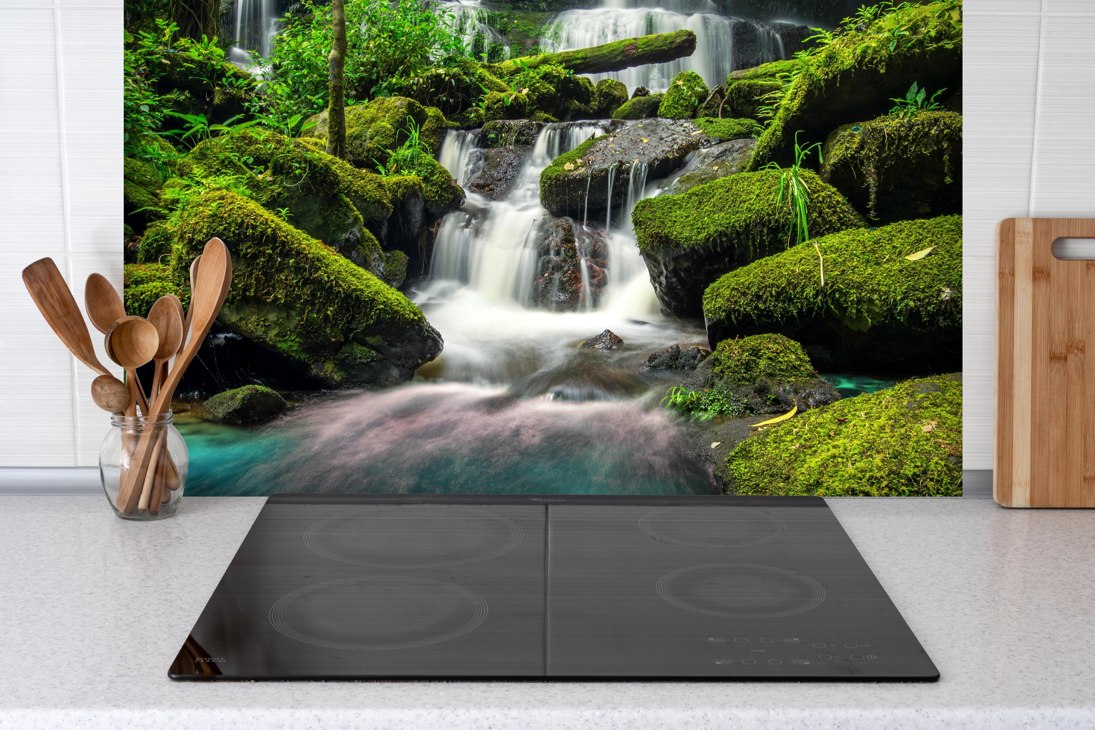 Spritzschutz - Wasserfall im grünen Dschungel von Thailand hinter einem Cerankochfeld zwischen Holz-Kochutensilien