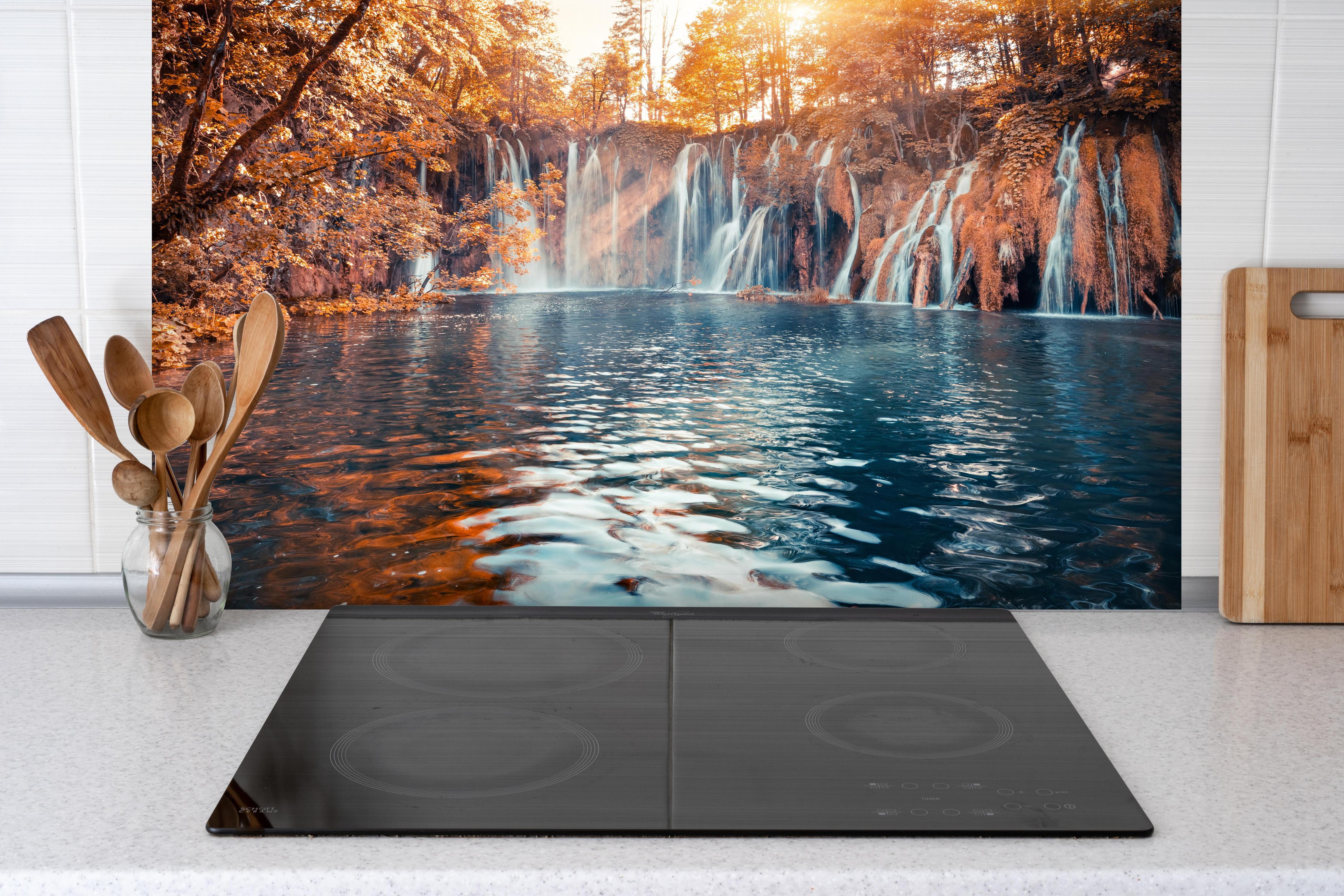 Spritzschutz - Wasserfall in Plitvice Nation bei Sonnenaufgang hinter einem Cerankochfeld zwischen Holz-Kochutensilien