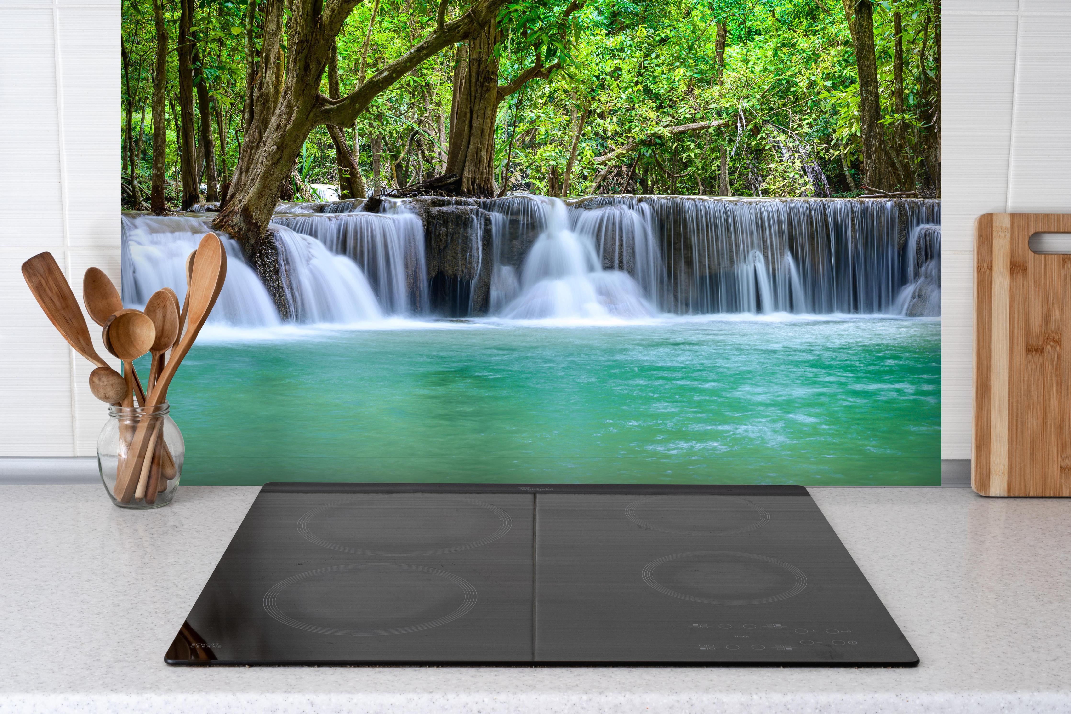 Spritzschutz - Wasserfall tief im tropischen Wald hinter einem Cerankochfeld zwischen Holz-Kochutensilien