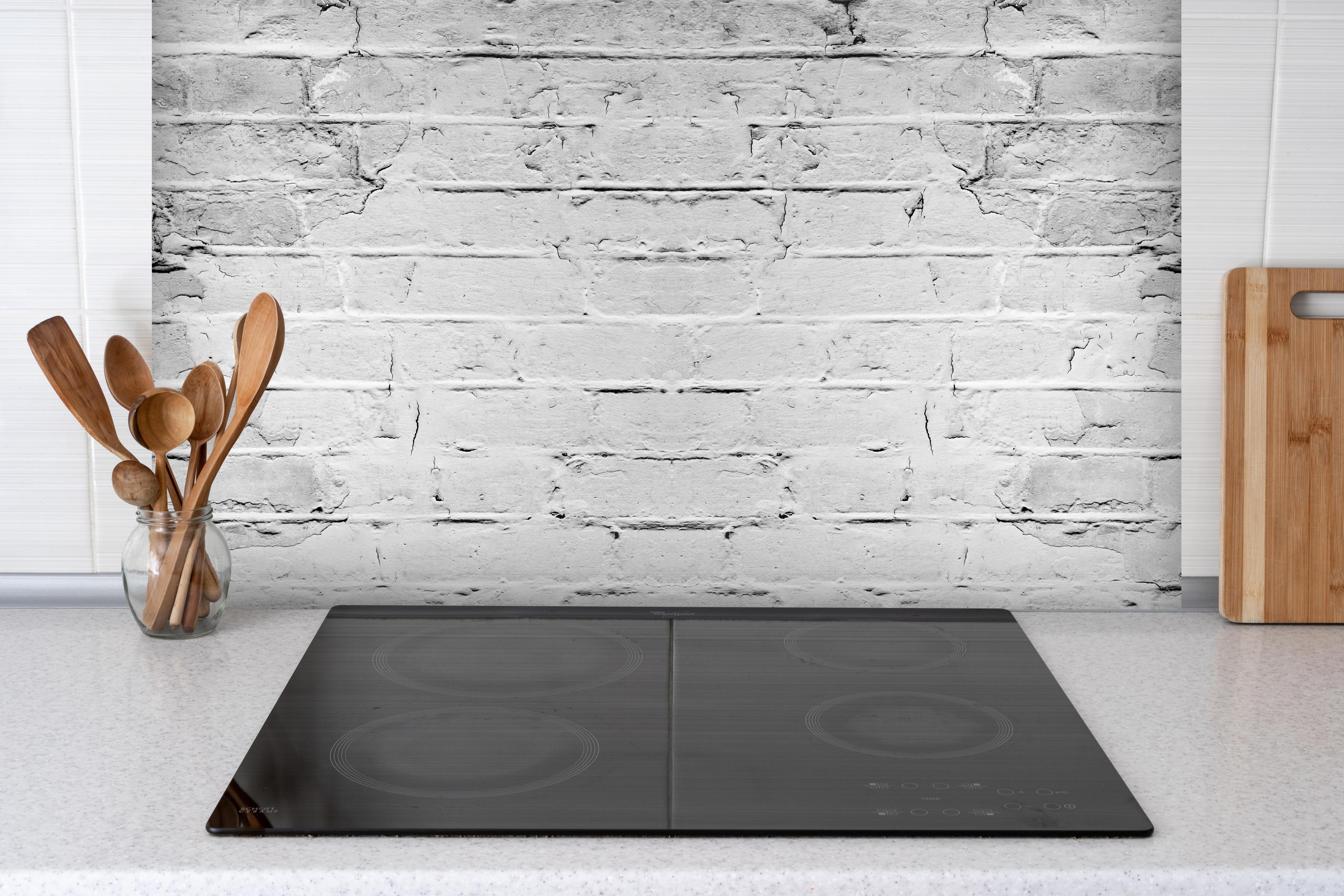 Spritzschutz - Weiß grau beschädigte Backstein Wand hinter einem Cerankochfeld zwischen Holz-Kochutensilien