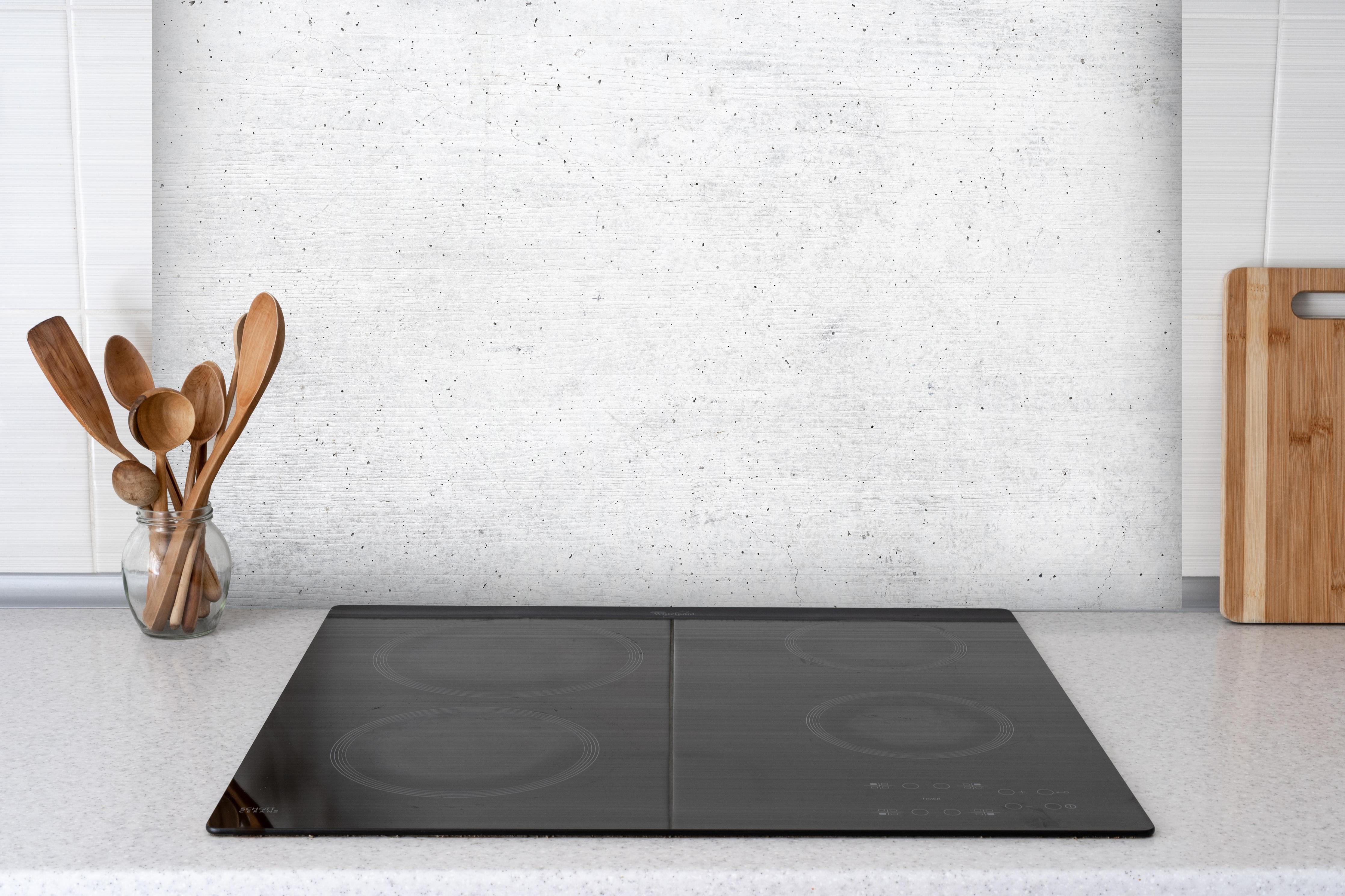 Spritzschutz - Weiße historische Betonwand hinter einem Cerankochfeld zwischen Holz-Kochutensilien