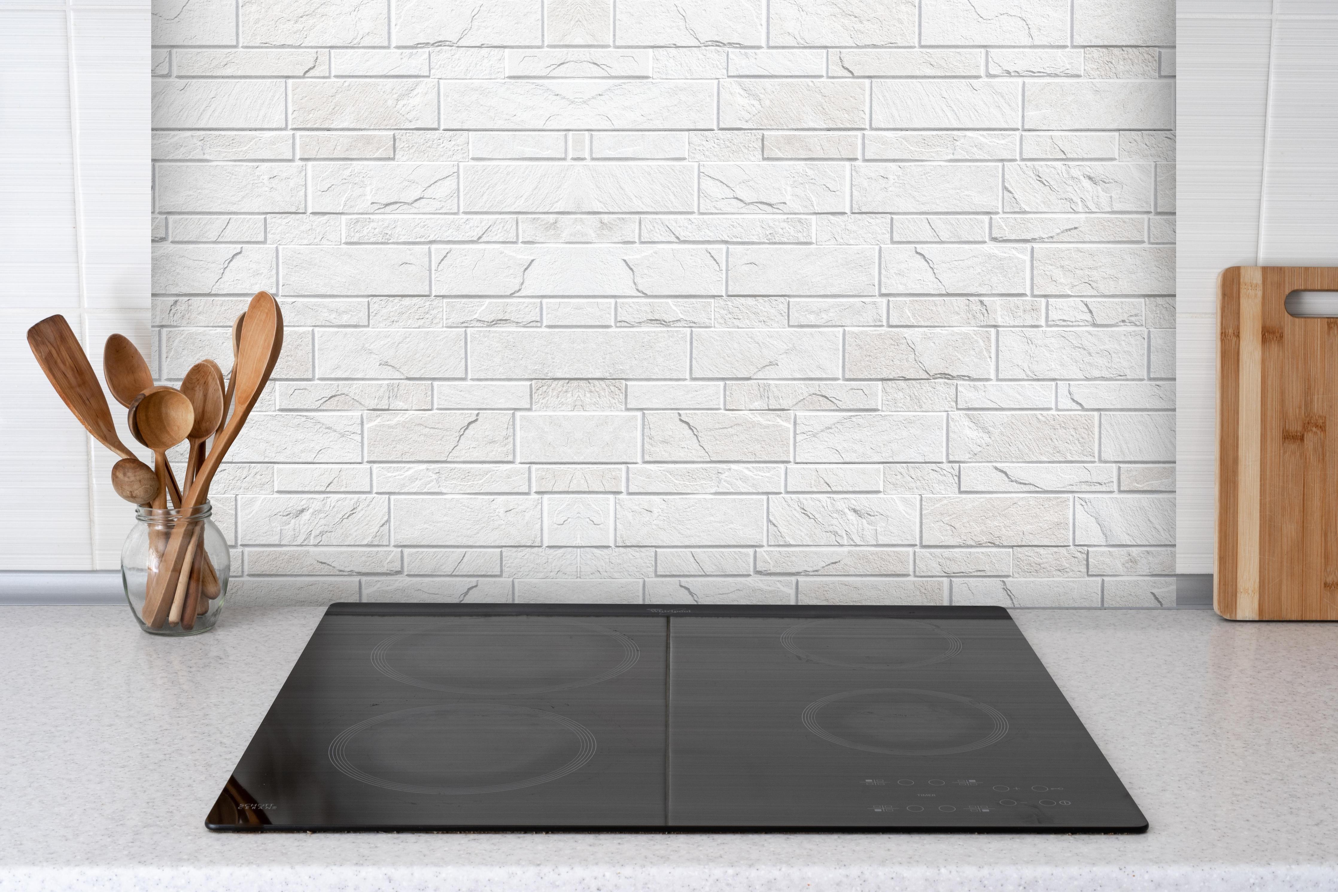 Spritzschutz - Weiße moderne Steinwand hinter einem Cerankochfeld zwischen Holz-Kochutensilien