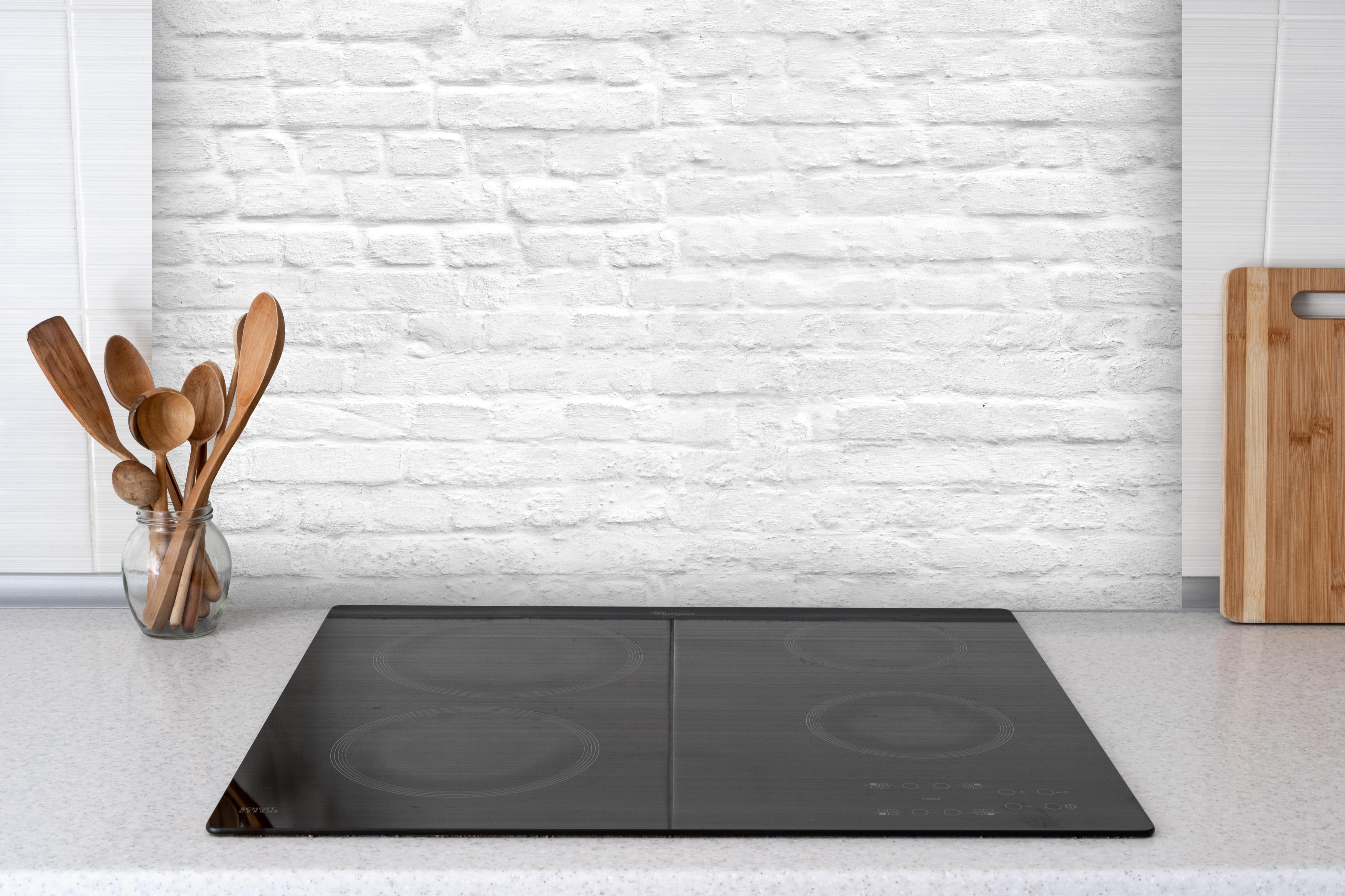 Spritzschutz - Weiße nahtlose Backsteinmauer hinter einem Cerankochfeld zwischen Holz-Kochutensilien