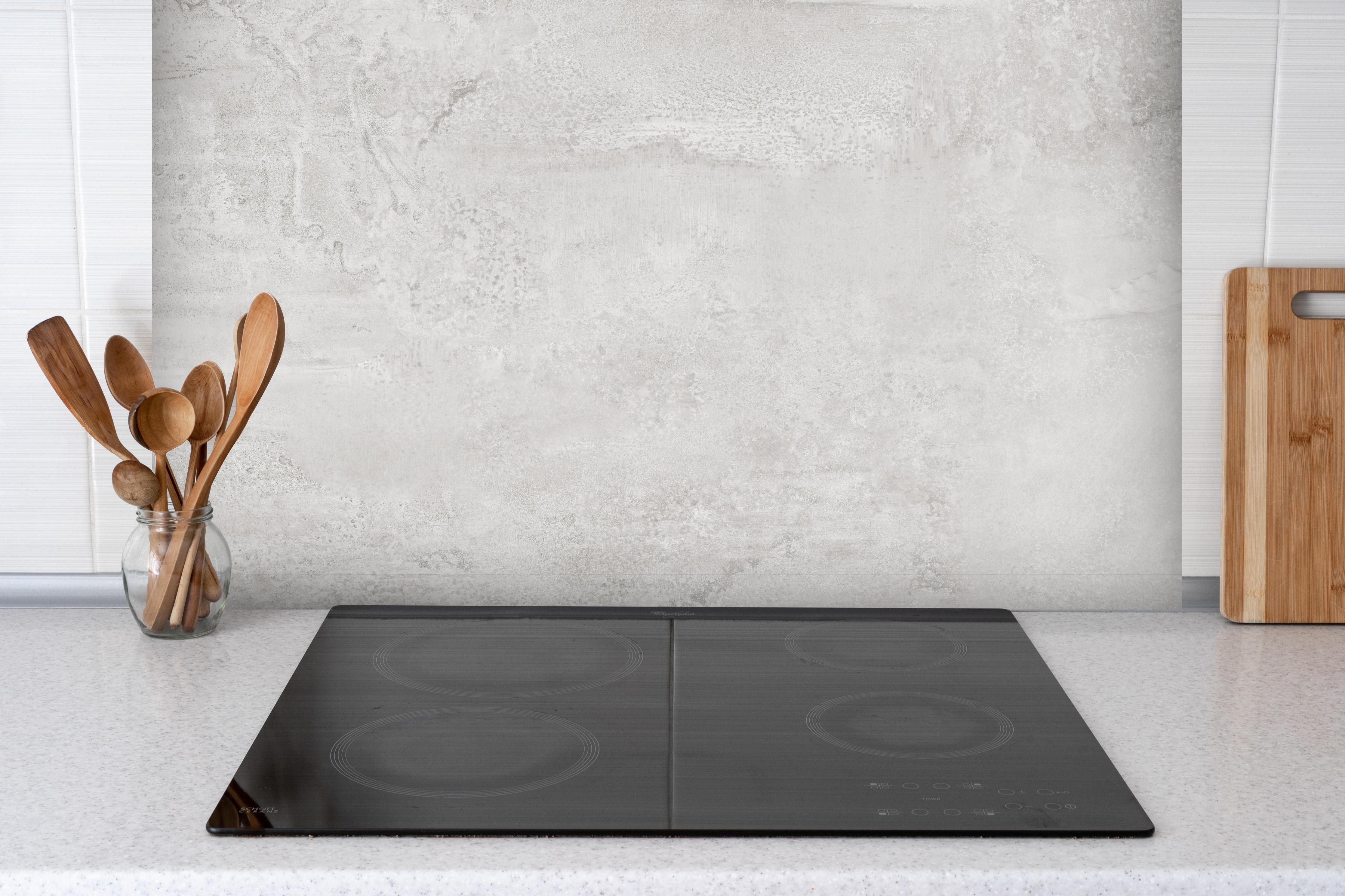 Spritzschutz - Weißer Wandhintergrund hinter einem Cerankochfeld zwischen Holz-Kochutensilien