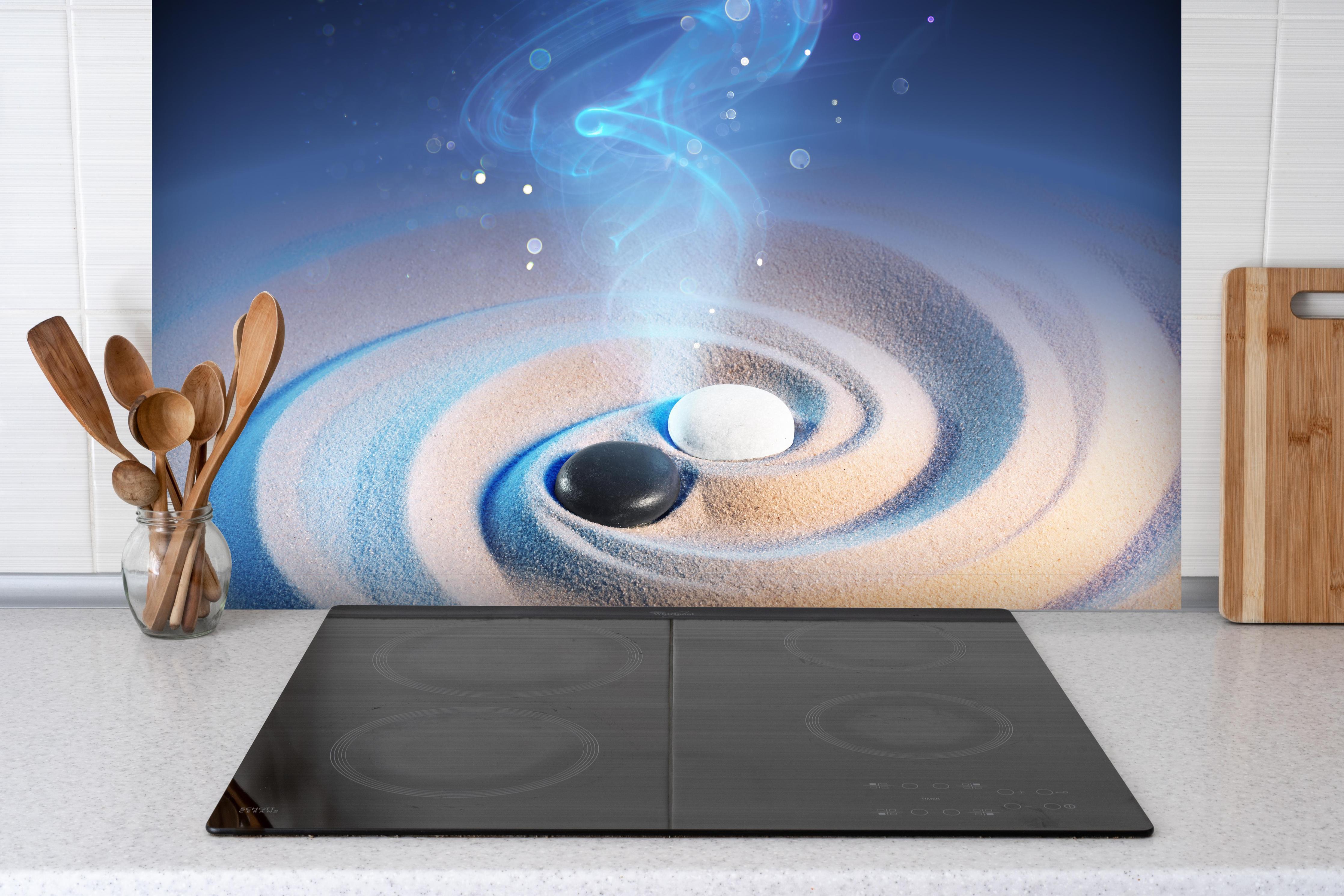 Spritzschutz - Yin und Yang Steine im Sand hinter einem Cerankochfeld zwischen Holz-Kochutensilien