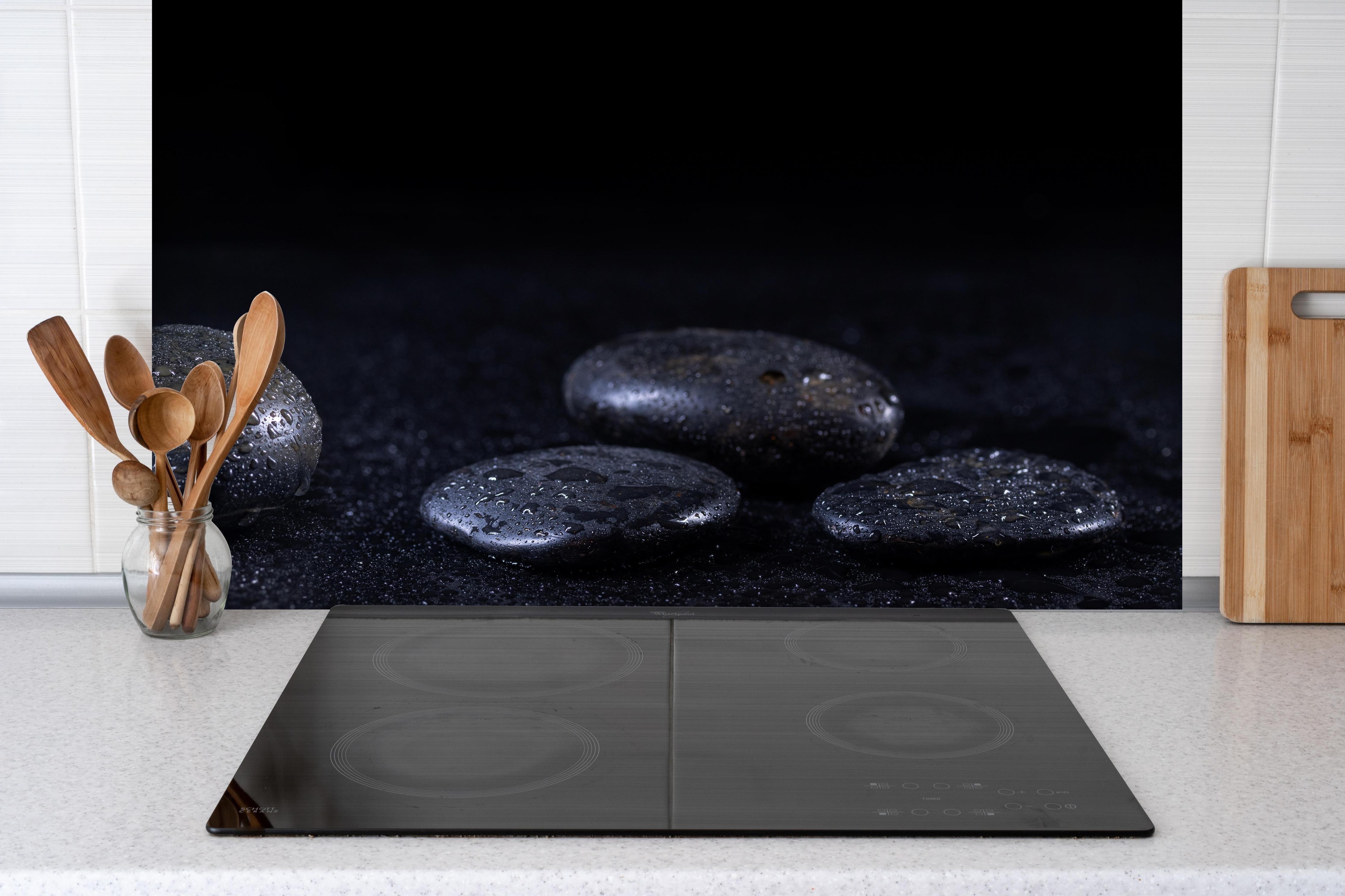 Spritzschutz - Zen - Schwarze Steine hinter einem Cerankochfeld zwischen Holz-Kochutensilien