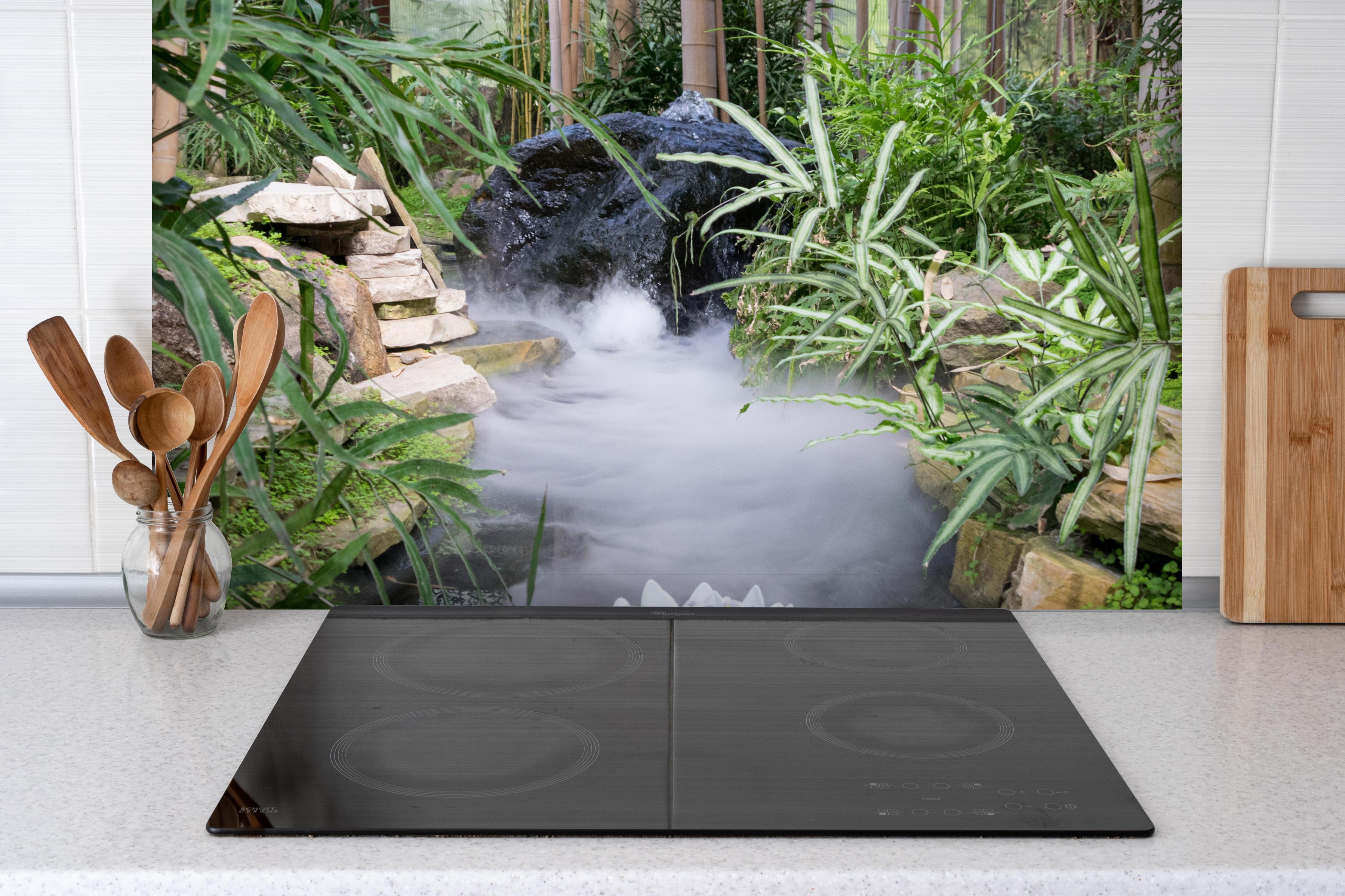 Spritzschutz - Zen-Garten mit weißer Seerose hinter einem Cerankochfeld zwischen Holz-Kochutensilien