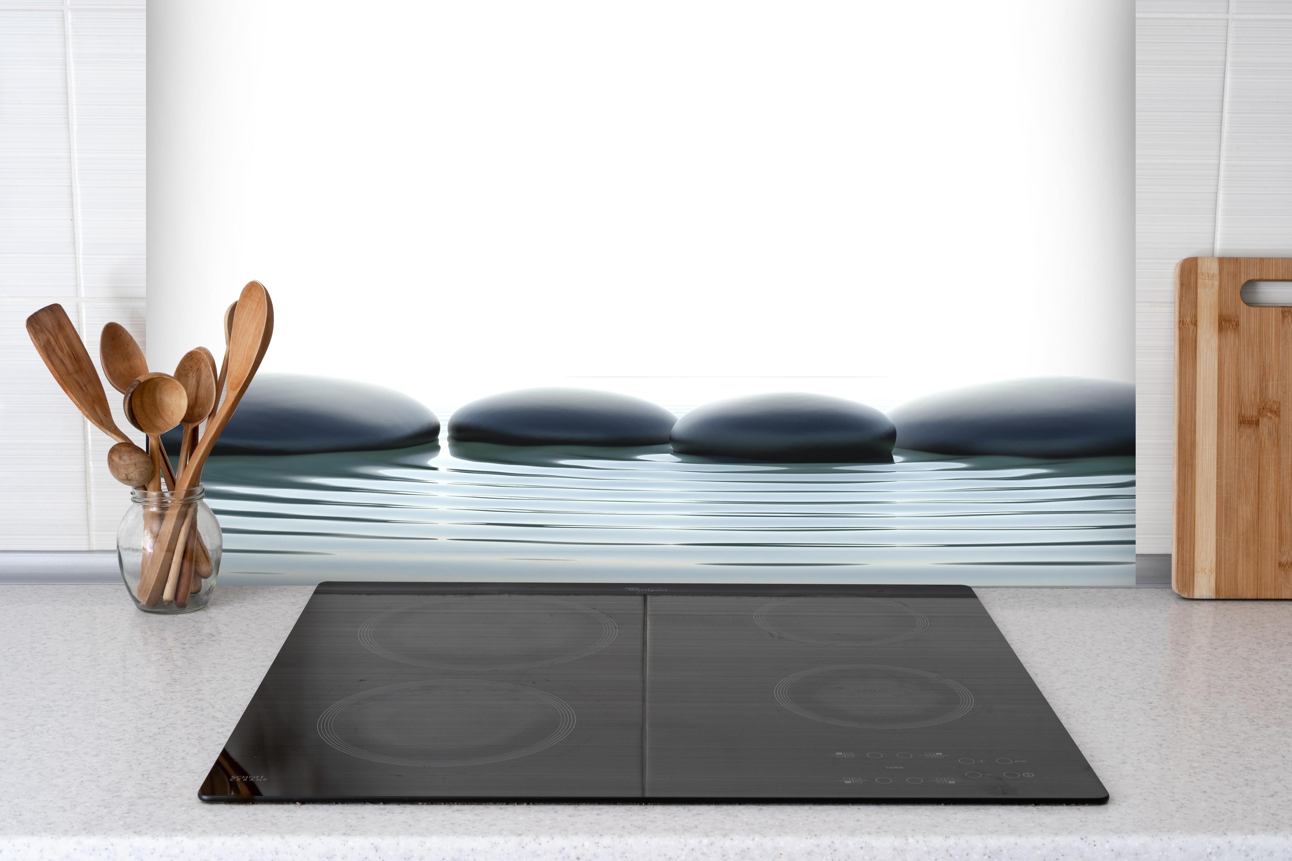 Spritzschutz - Zen-Steine im Wasser mit Wellen hinter einem Cerankochfeld zwischen Holz-Kochutensilien