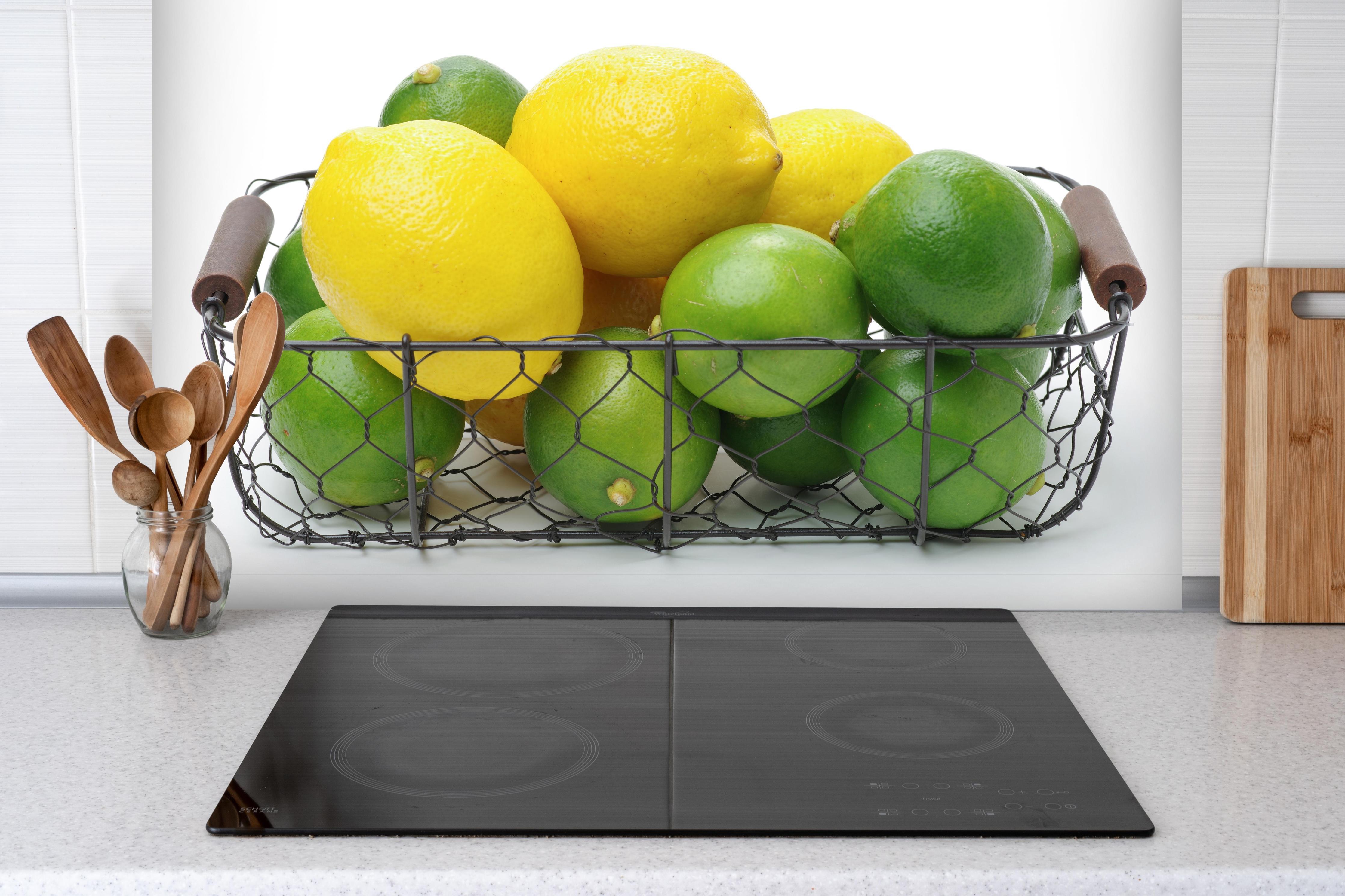 Spritzschutz - Zitrusfrüchte im Korb hinter einem Cerankochfeld zwischen Holz-Kochutensilien