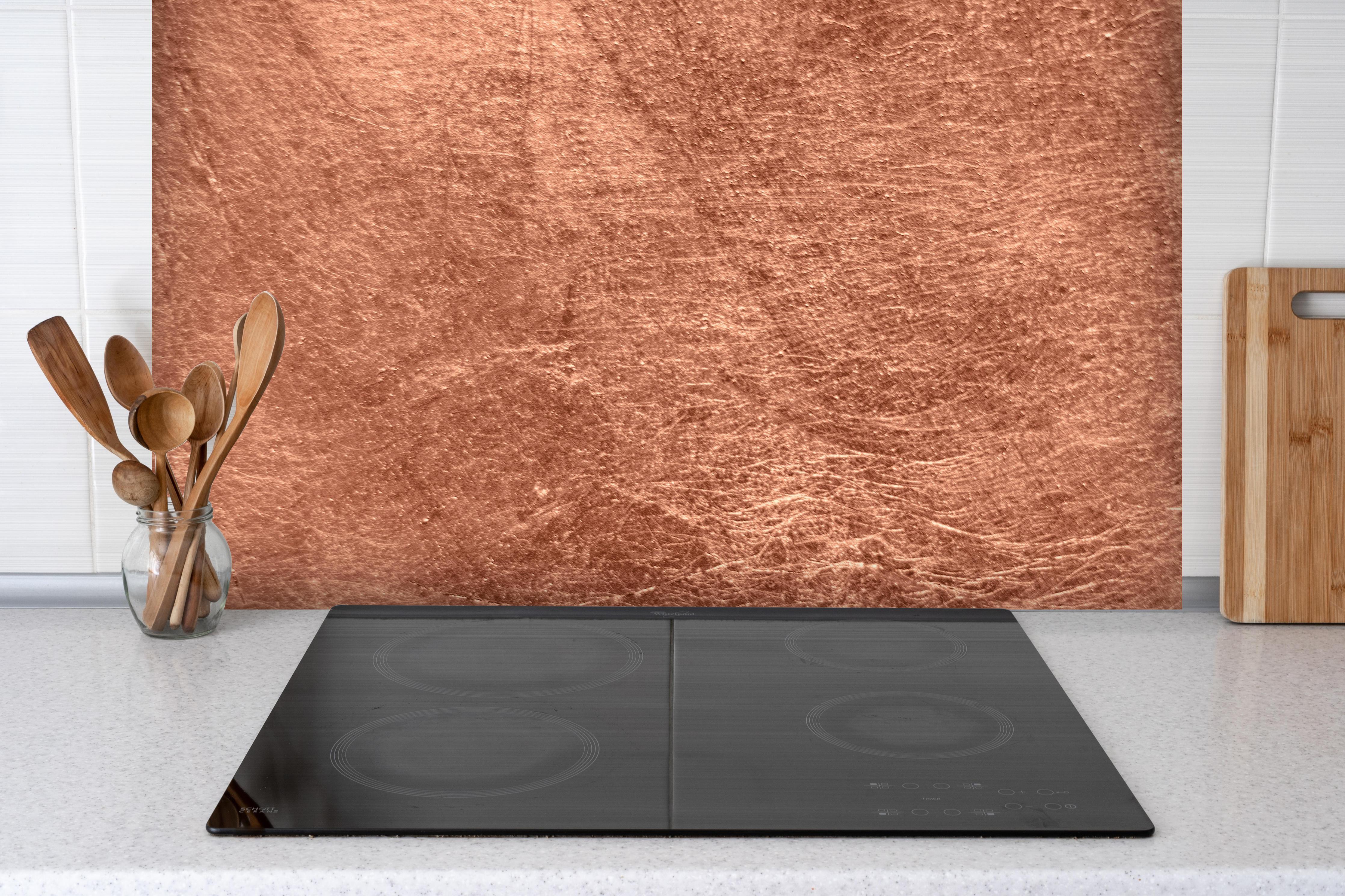 Spritzschutz - gebürstetes belichtetes Kupfer hinter einem Cerankochfeld zwischen Holz-Kochutensilien