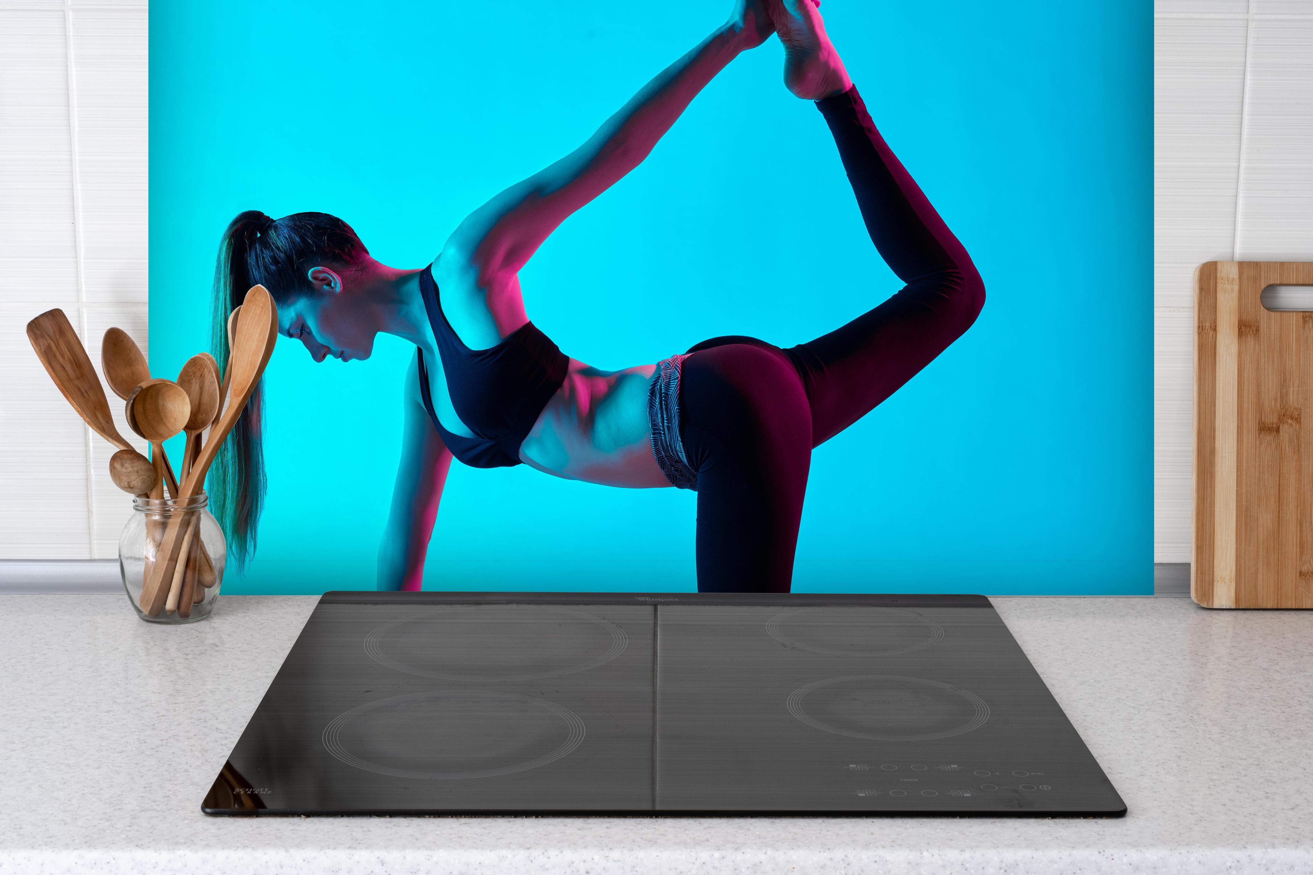 Spritzschutz - konzentrierte Frau in Yoga-Pose hinter einem Cerankochfeld zwischen Holz-Kochutensilien