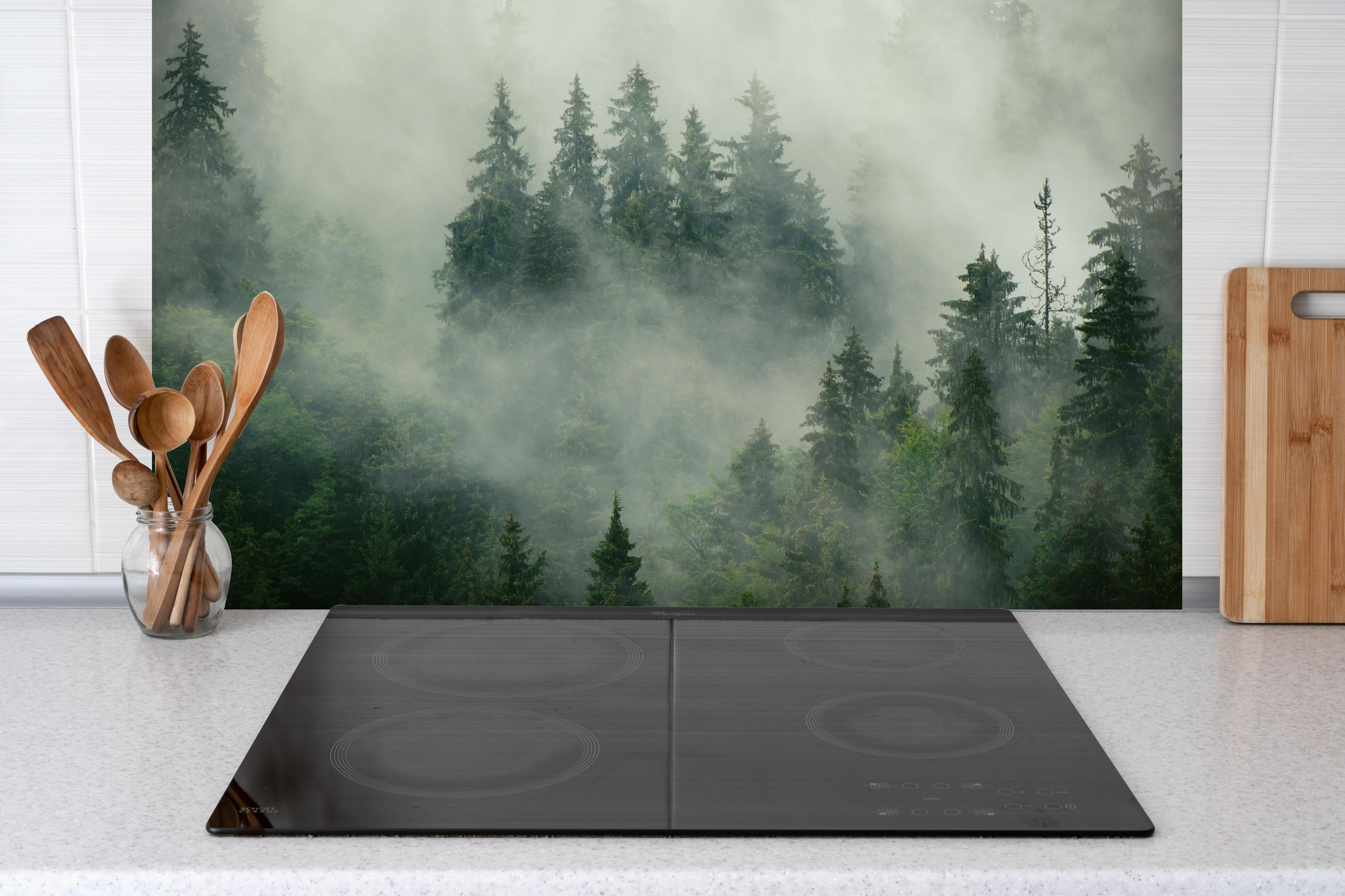 Spritzschutz - neblige Waldlandschaft hinter einem Cerankochfeld zwischen Holz-Kochutensilien