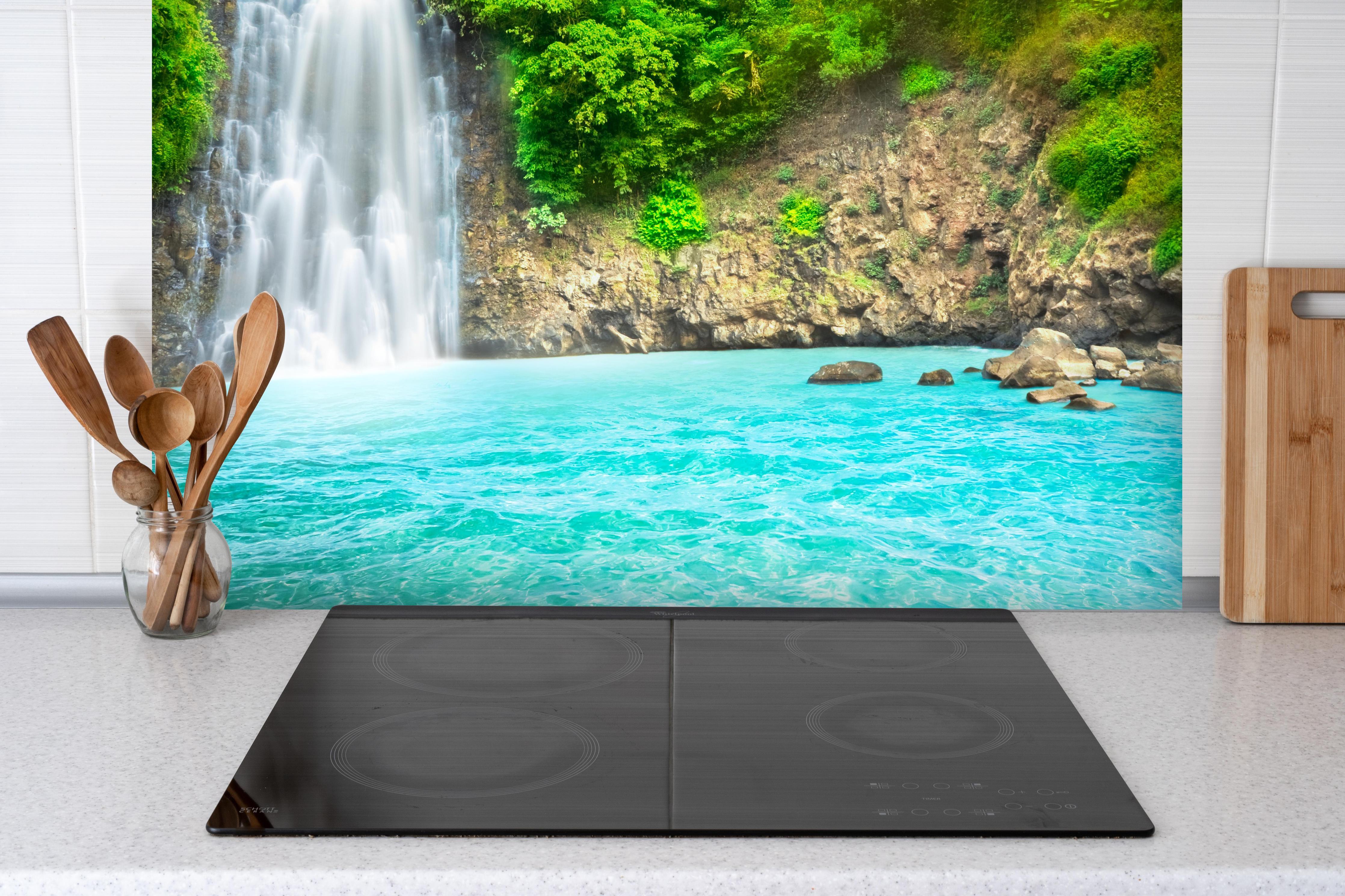 Spritzschutz - tropischer Wasserfall hinter einem Cerankochfeld zwischen Holz-Kochutensilien