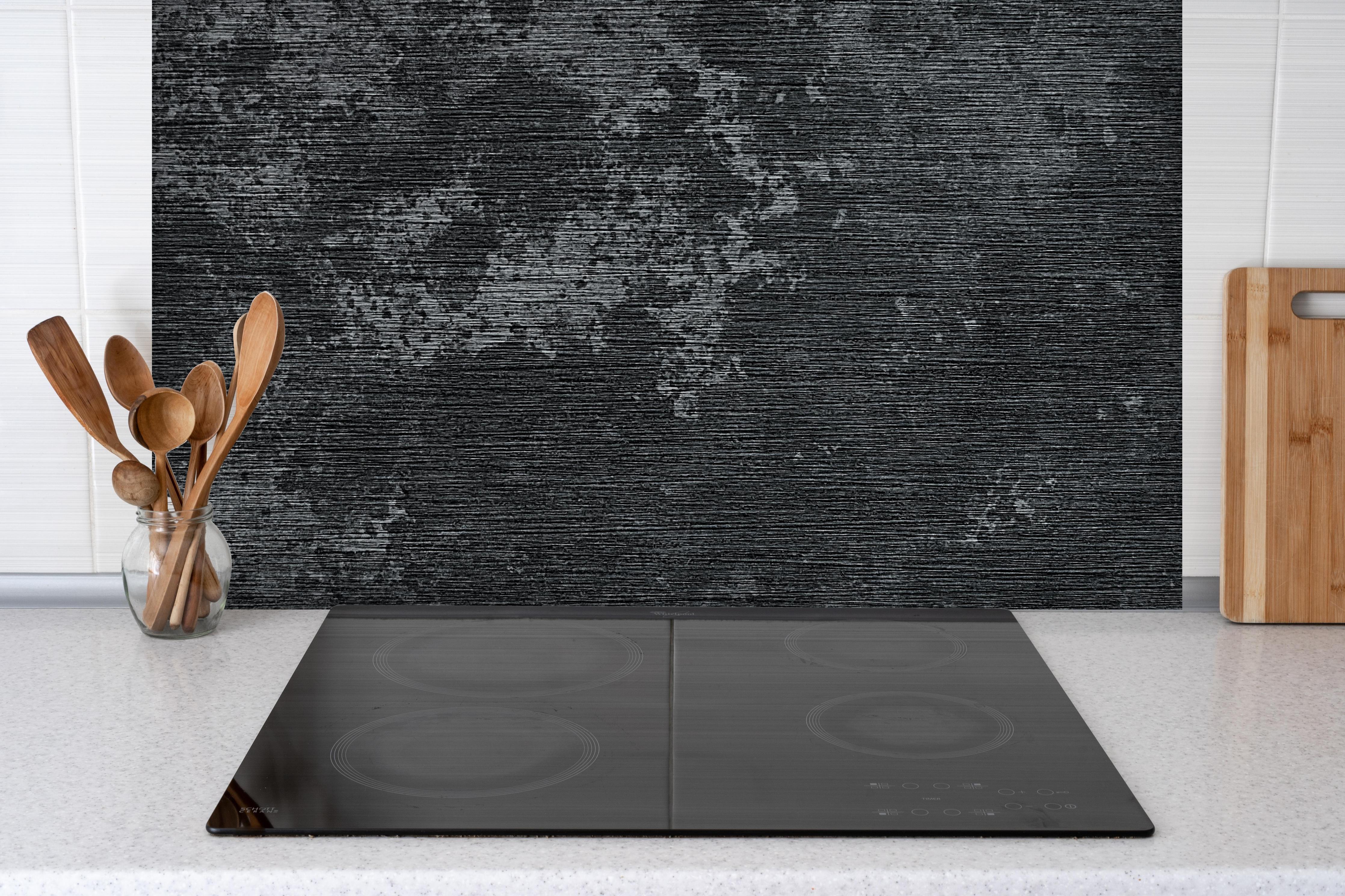 Spritzschutz - wild gebürstetes Metall hinter einem Cerankochfeld zwischen Holz-Kochutensilien