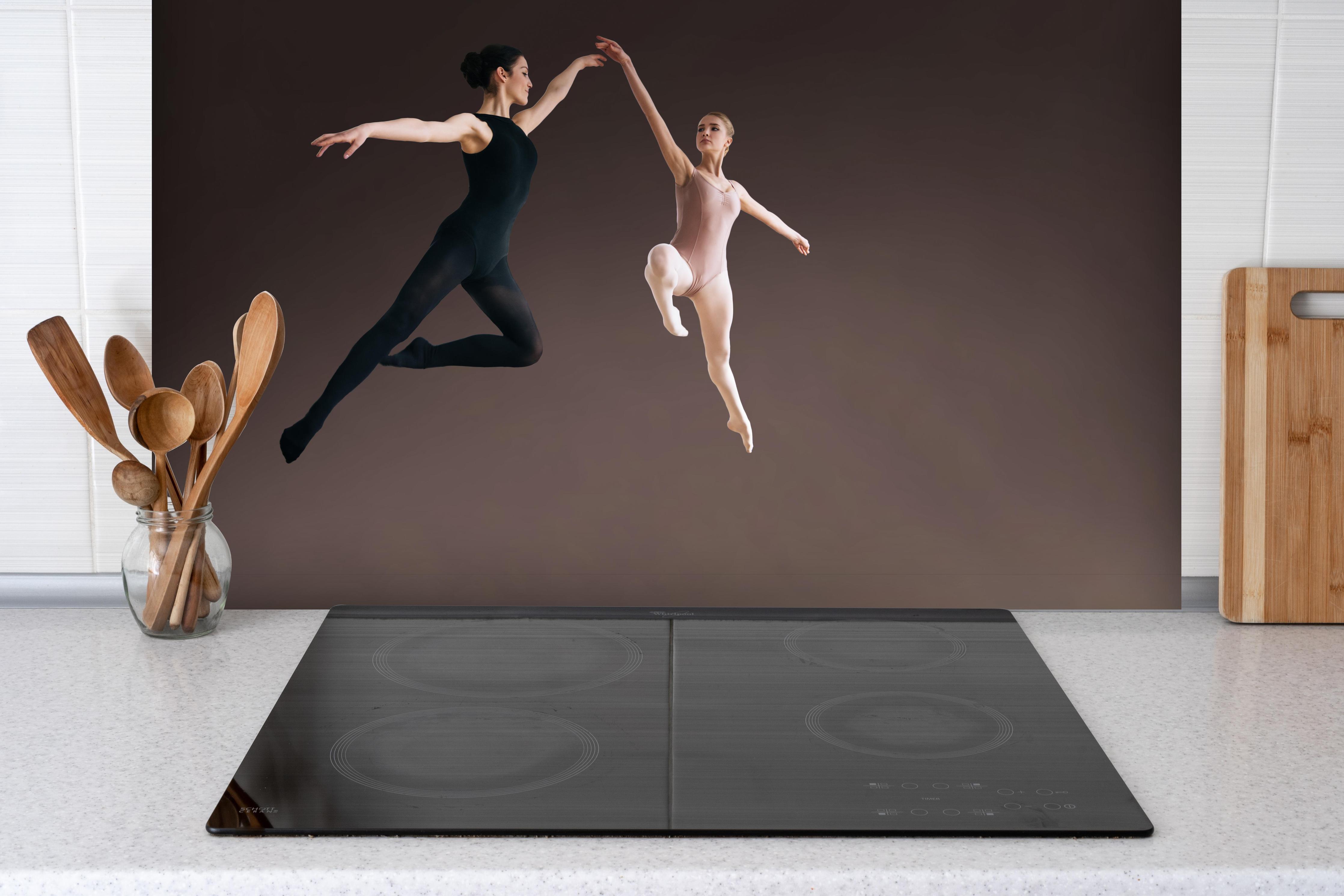 Spritzschutz - zwei Balletttänzerinnen hoch in der Luft hinter einem Cerankochfeld zwischen Holz-Kochutensilien