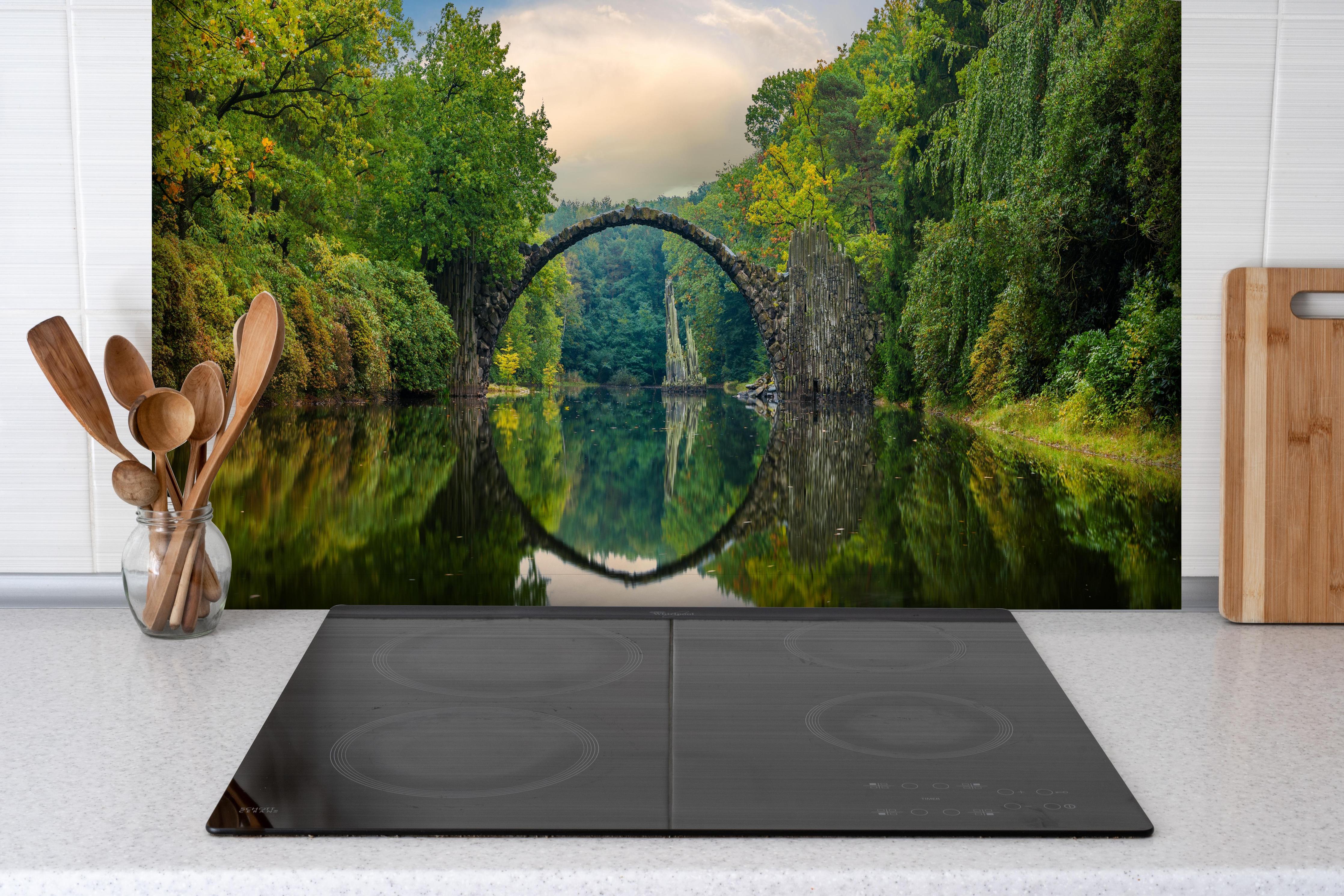 Spritzschutz - Steinbrücke über Fluss im Wald hinter einem Cerankochfeld zwischen Holz-Kochutensilien