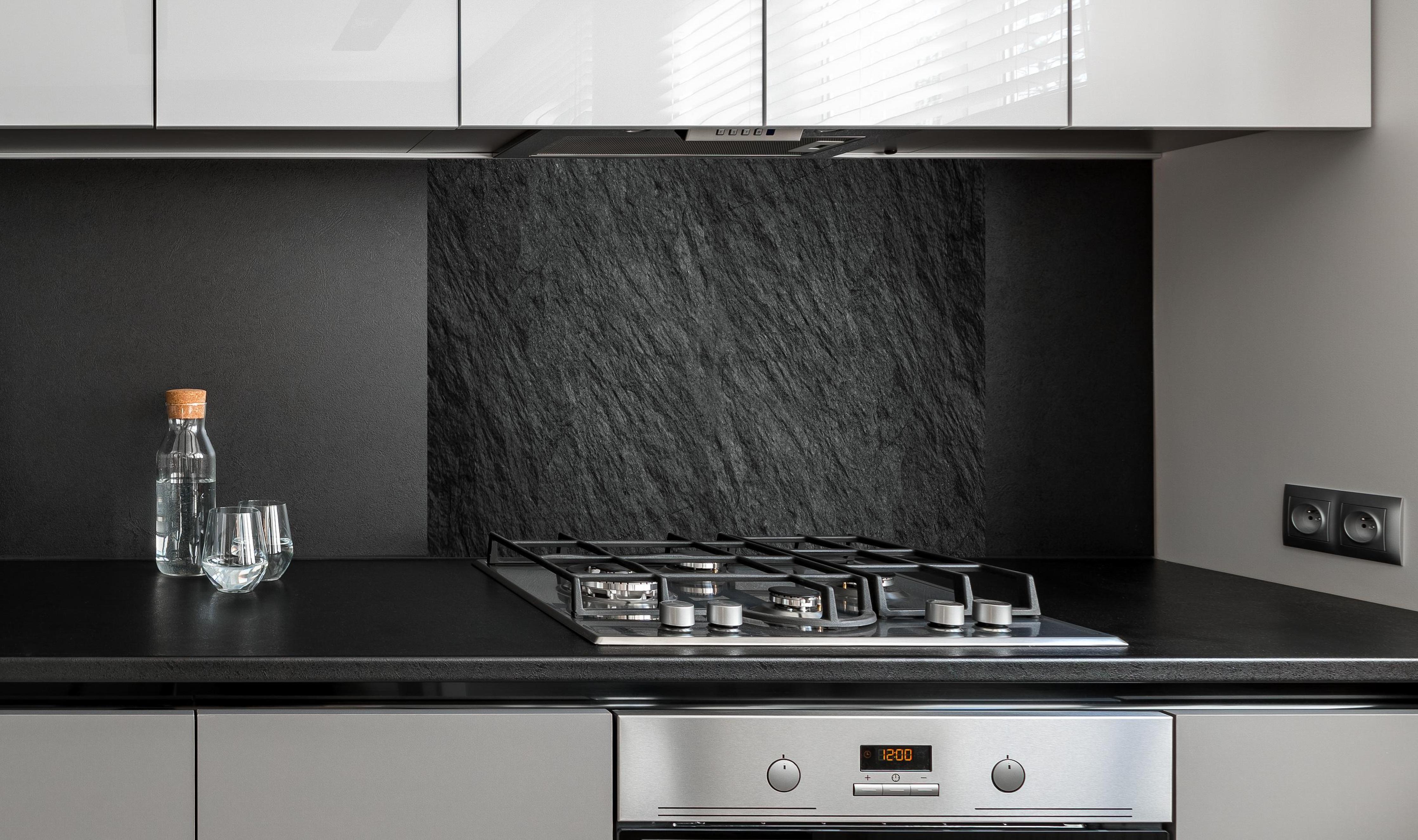 Spritzschutz - Steintextur mit Rissen hinter einem Cerankochfeld zwischen Holz-Kochutensilien