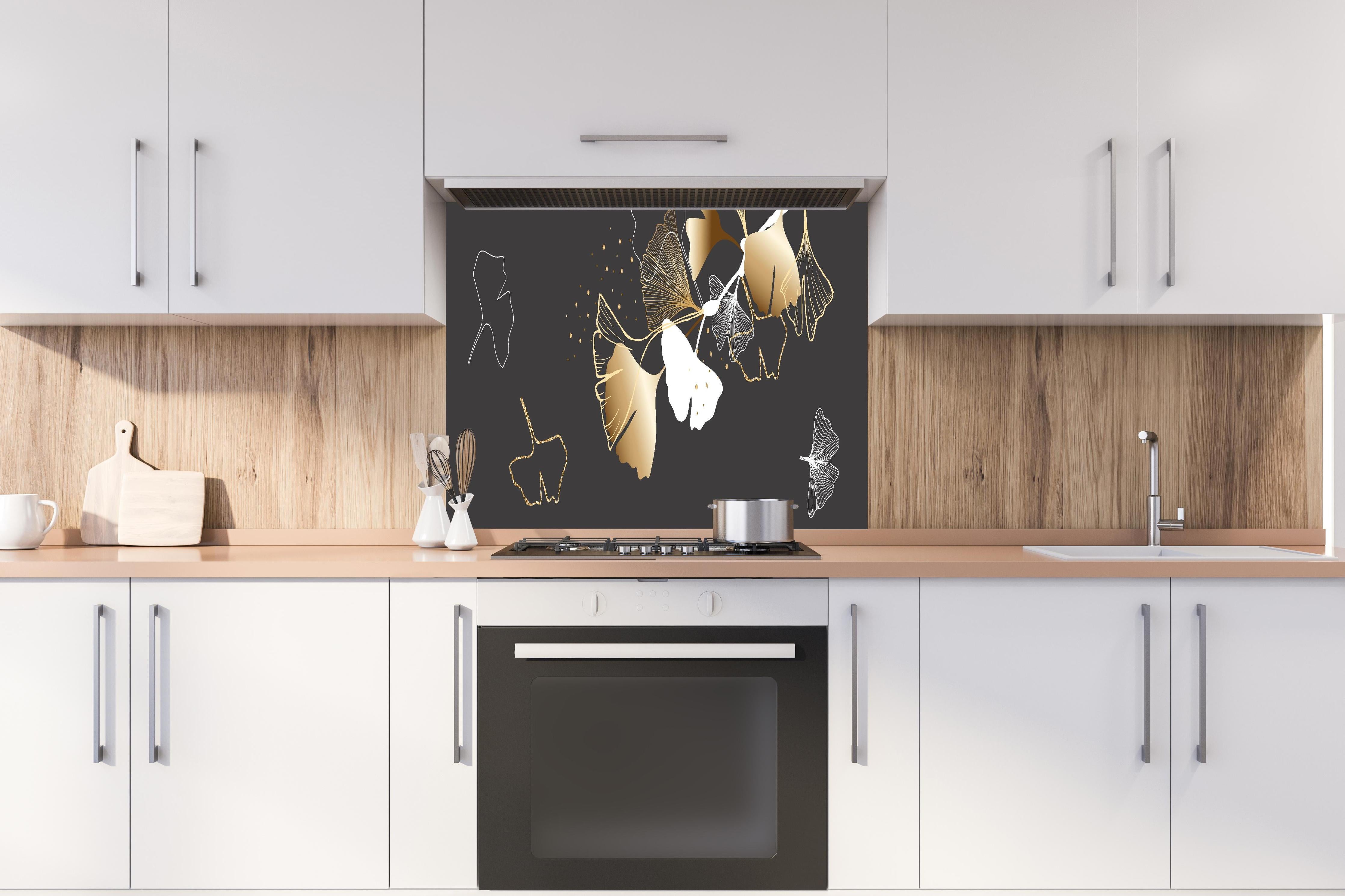 Spritzschutz - Stilisiertes Ginkgo-Design in Gold und Schwarz hinter einem Cerankochfeld zwischen Holz-Kochutensilien