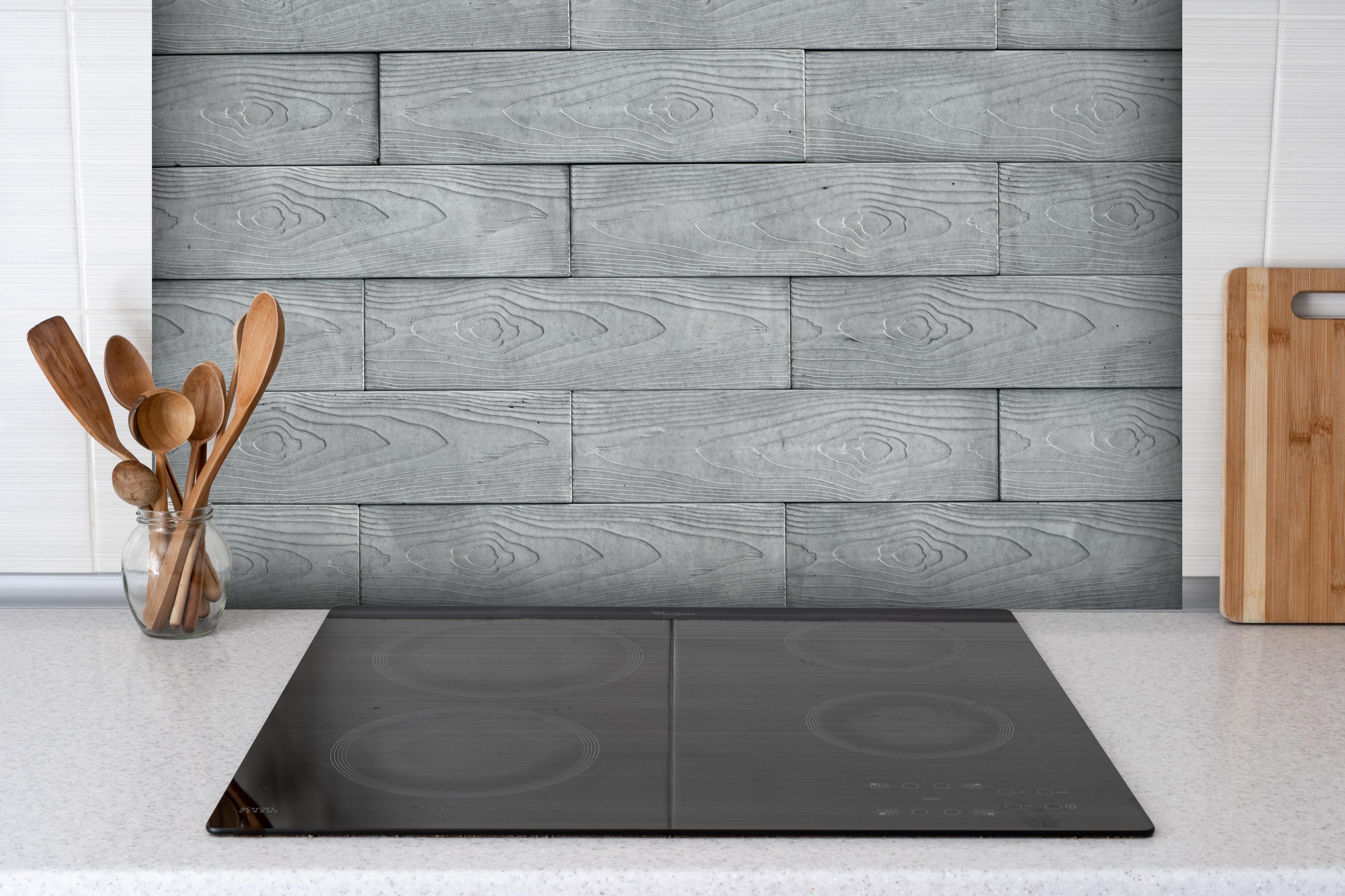 Spritzschutz - Stilvolle weiße Holzstruktur mit Grautönen hinter einem Cerankochfeld zwischen Holz-Kochutensilien