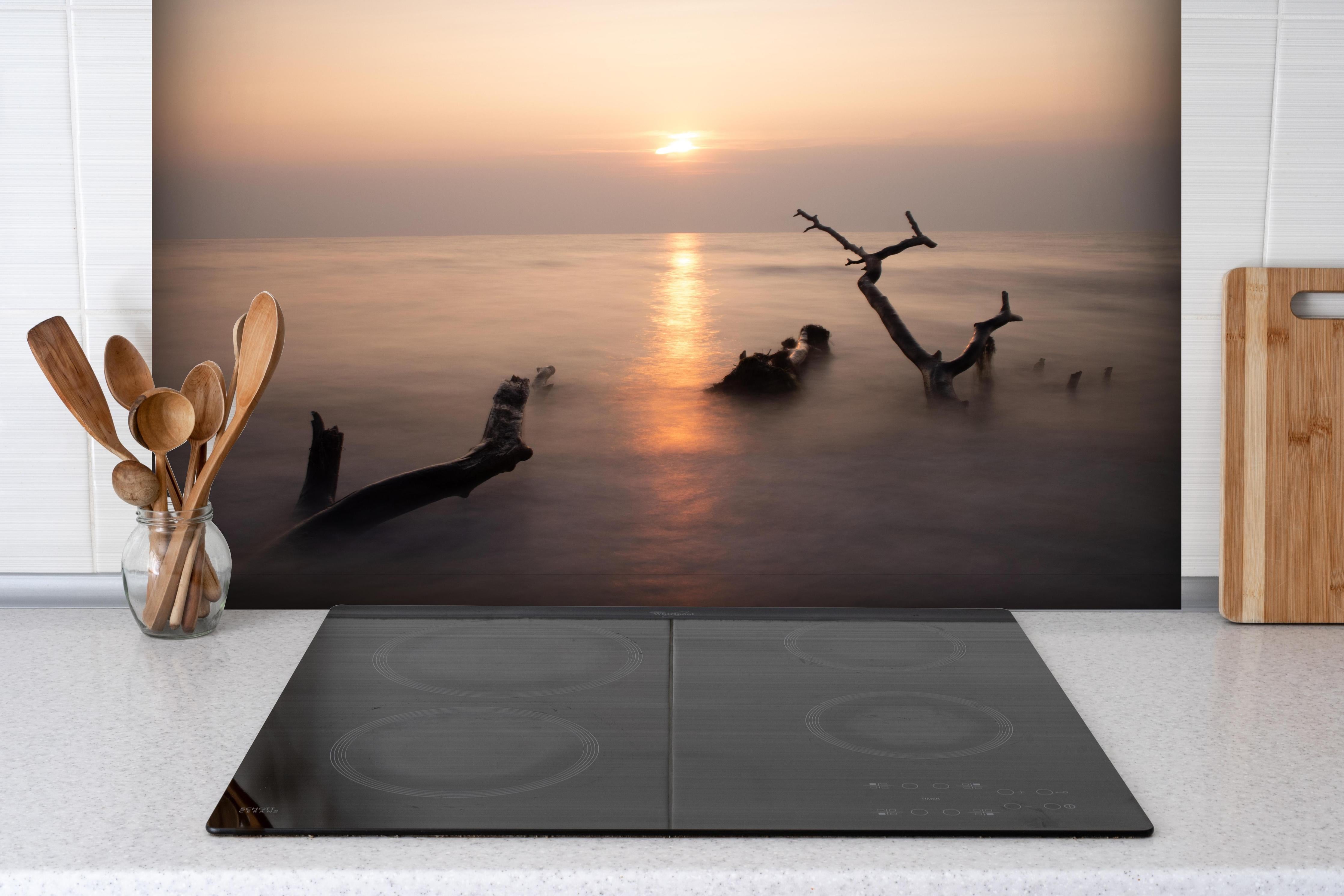 Spritzschutz - Stimmungsvoller Sonnenuntergangs-Strand hinter einem Cerankochfeld zwischen Holz-Kochutensilien