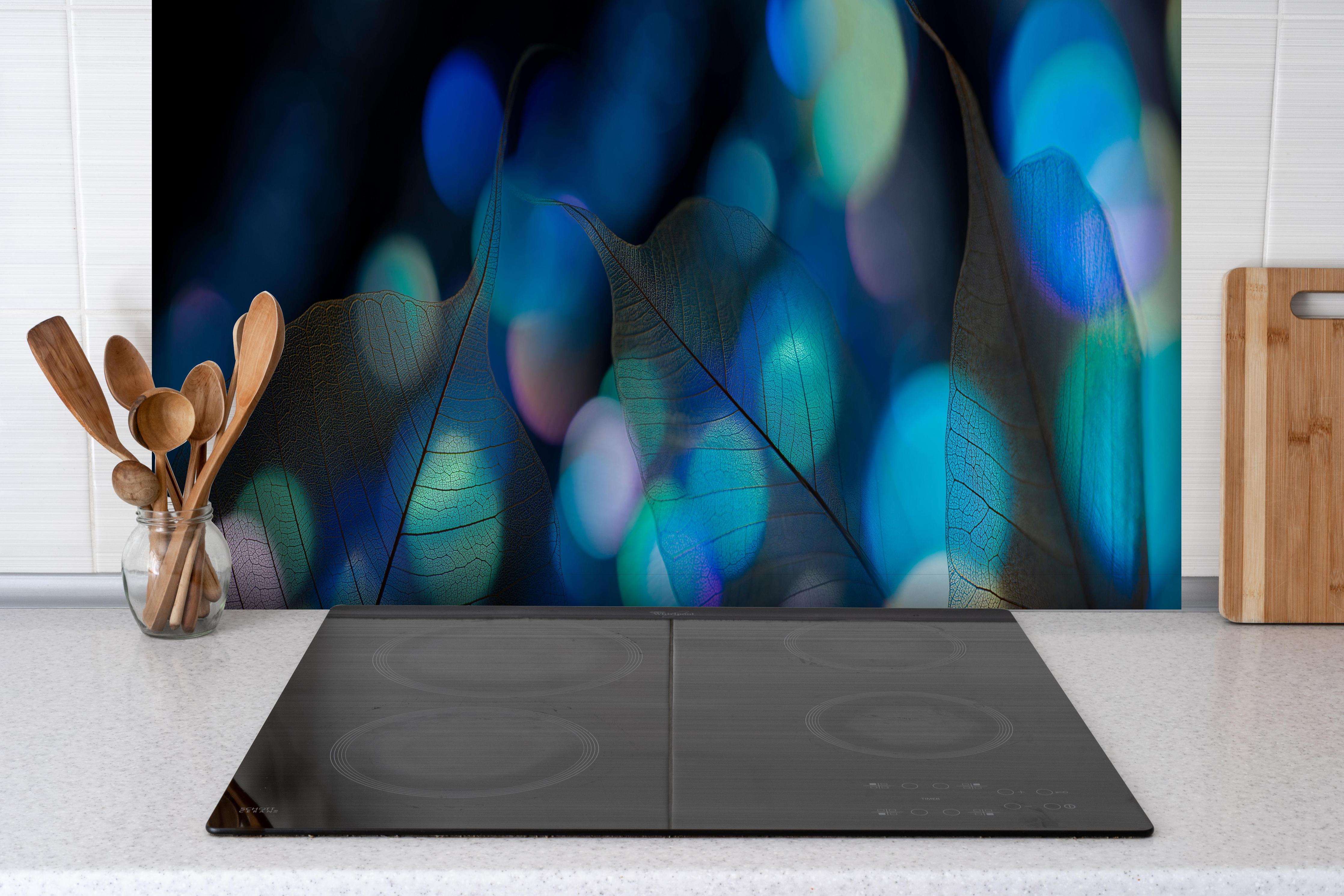Spritzschutz - Strahlende Blattstruktur mit blauem Licht hinter einem Cerankochfeld zwischen Holz-Kochutensilien