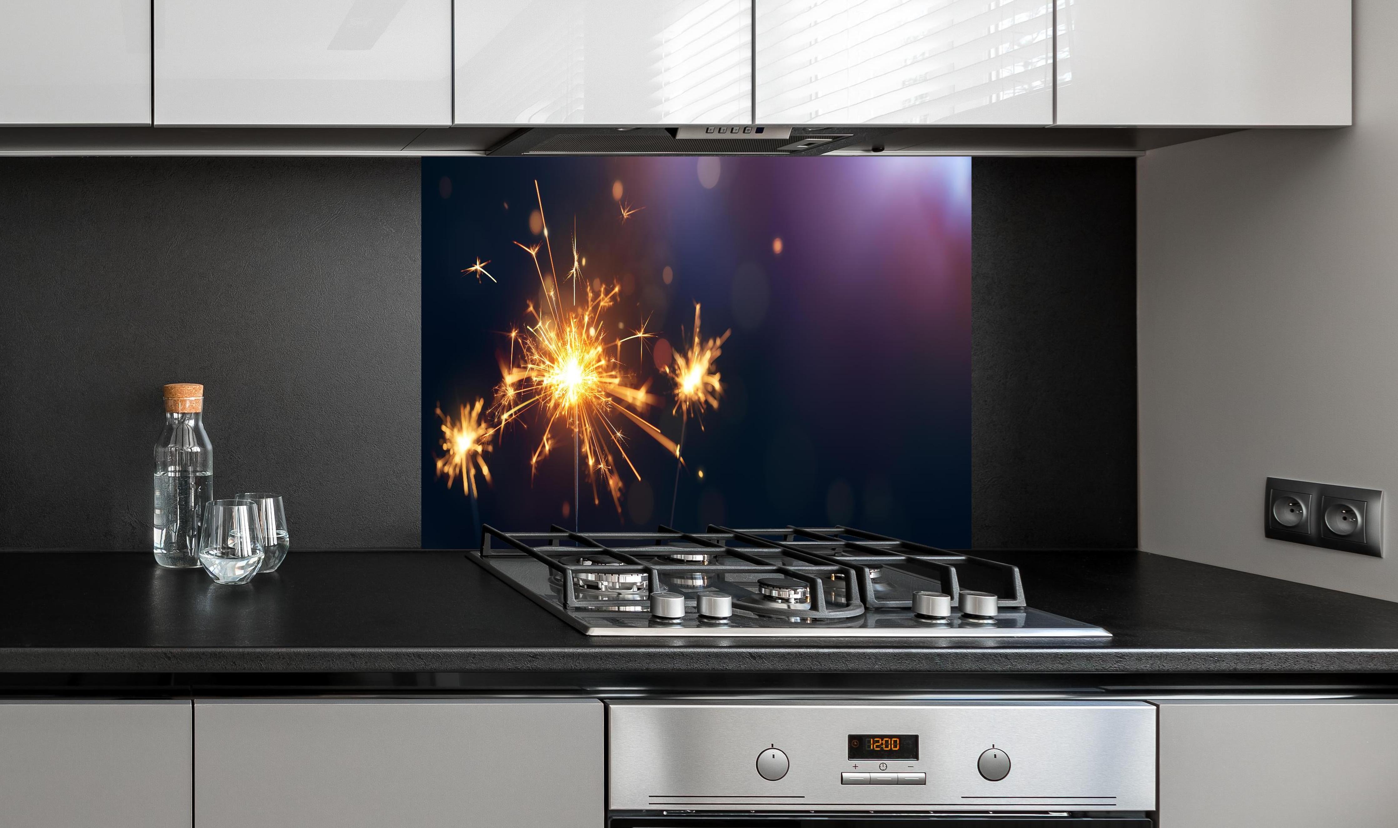 Spritzschutz - Strahlendes Wunderkerzen-Goldlichtfeuerwerk hinter einem Cerankochfeld zwischen Holz-Kochutensilien