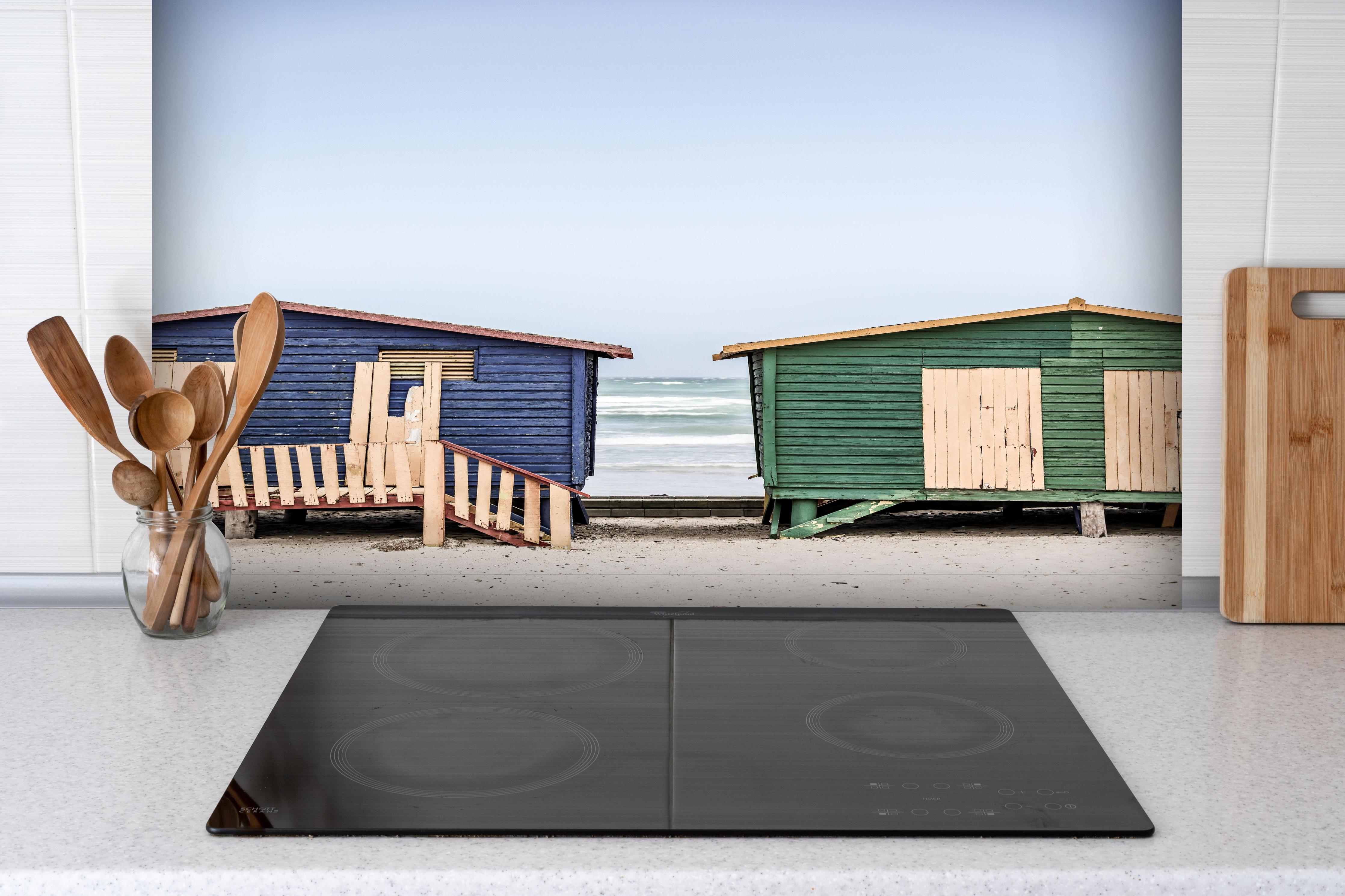 Spritzschutz - Strandhütten am Meer hinter einem Cerankochfeld zwischen Holz-Kochutensilien
