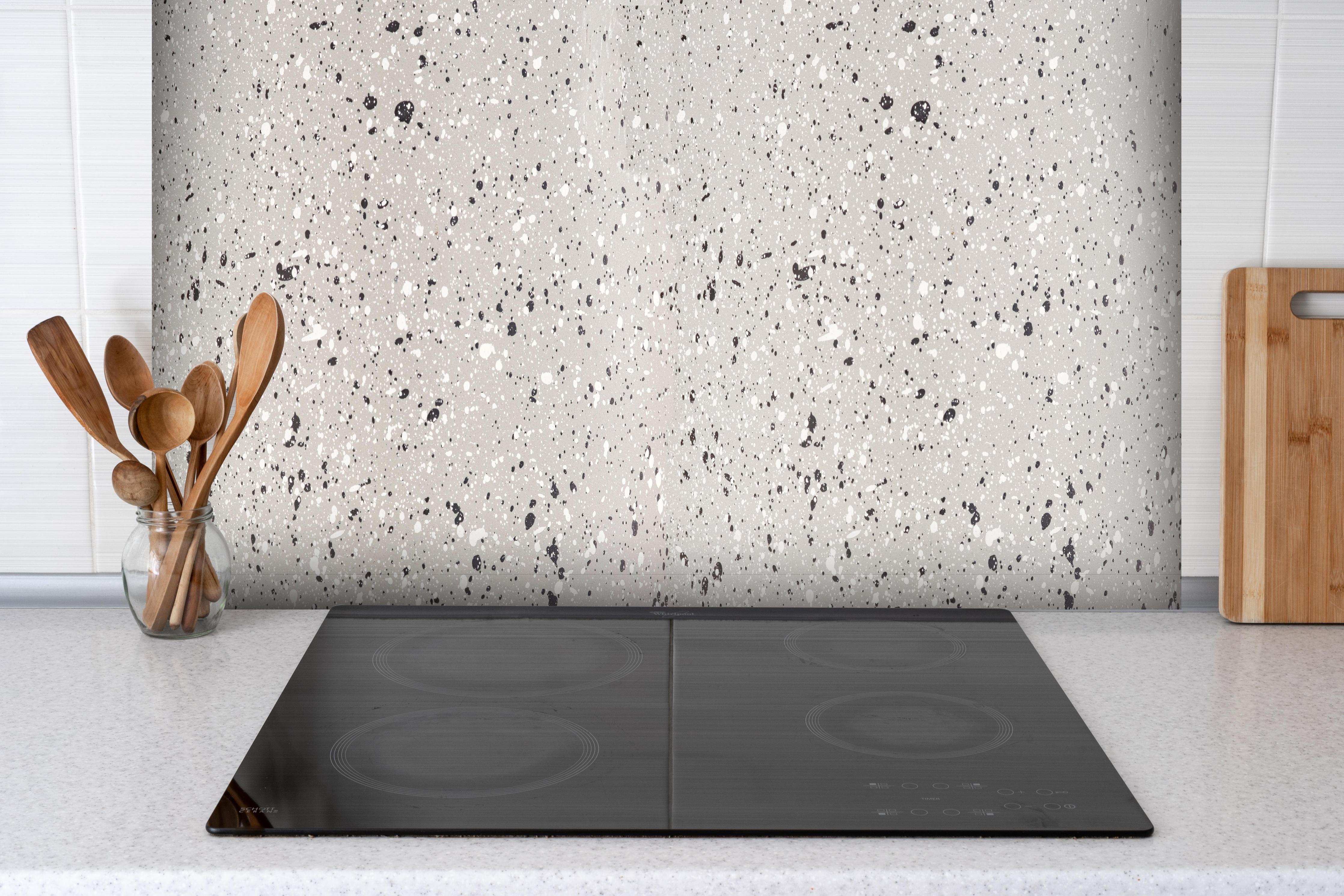 Spritzschutz - Terazzo Stein Textur - Nahaufnahme hinter einem Cerankochfeld zwischen Holz-Kochutensilien