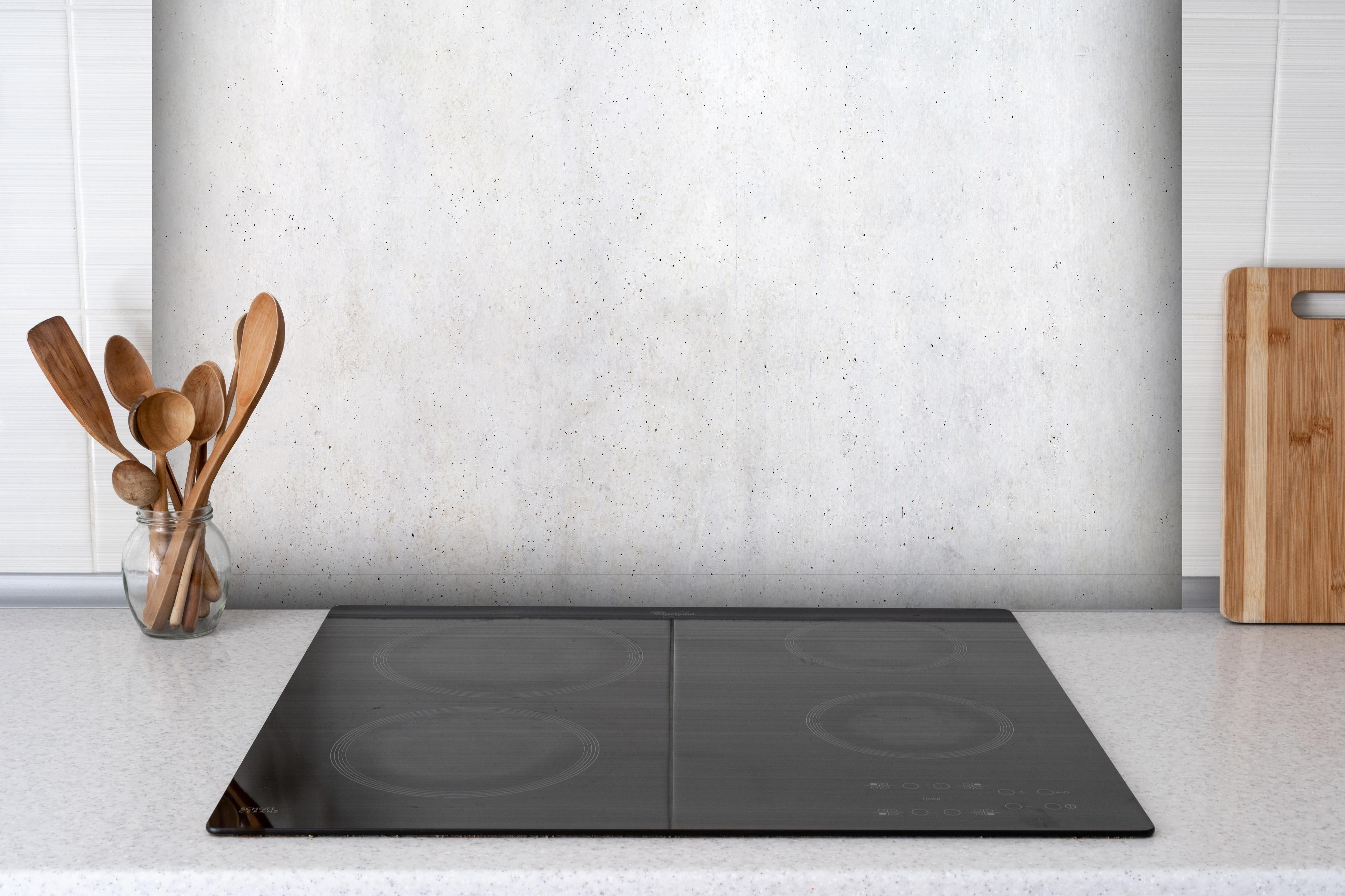 Spritzschutz - Textur einer weißen Betonwand hinter einem Cerankochfeld zwischen Holz-Kochutensilien