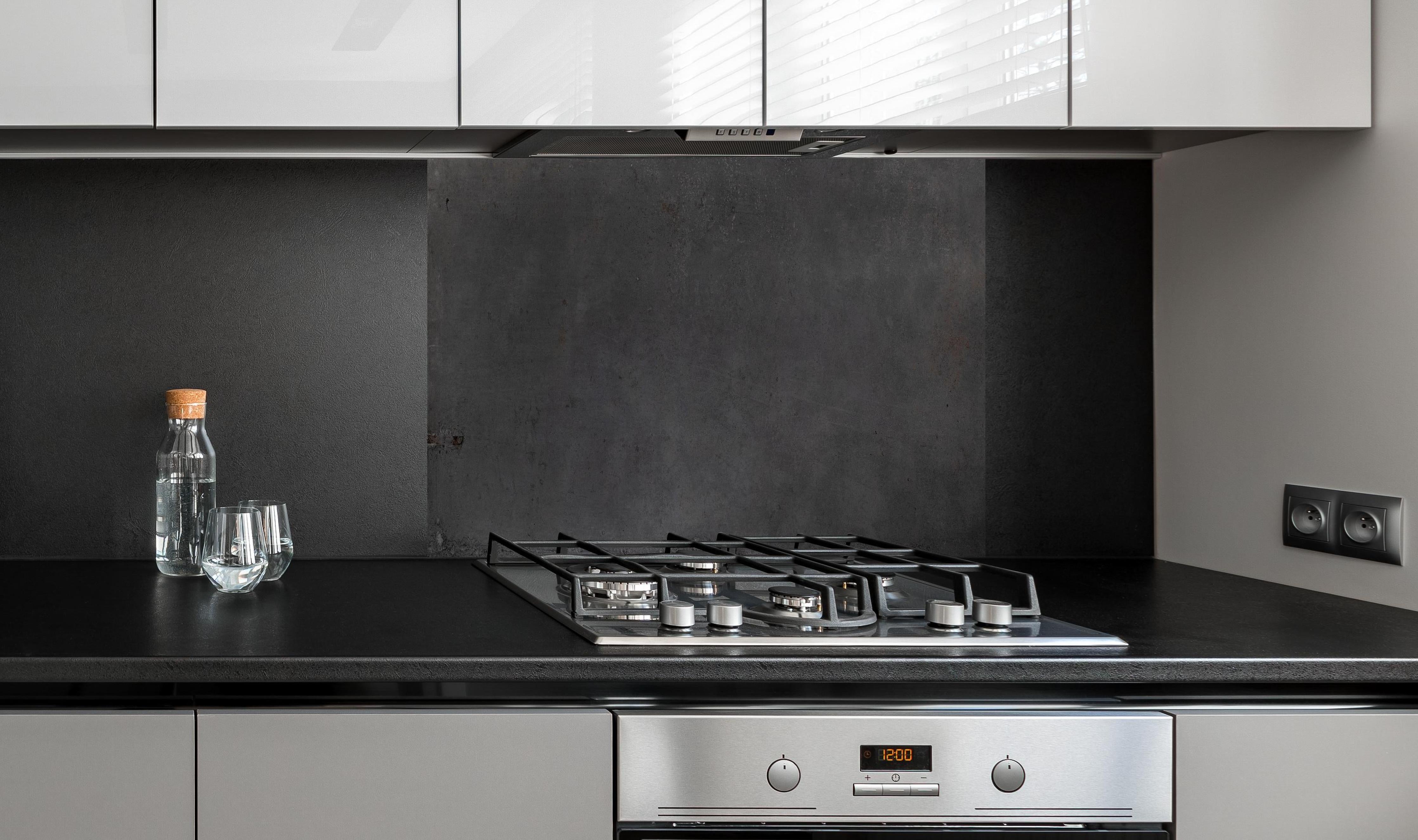 Spritzschutz - Textur von poliertem Beton hinter einem Cerankochfeld zwischen Holz-Kochutensilien