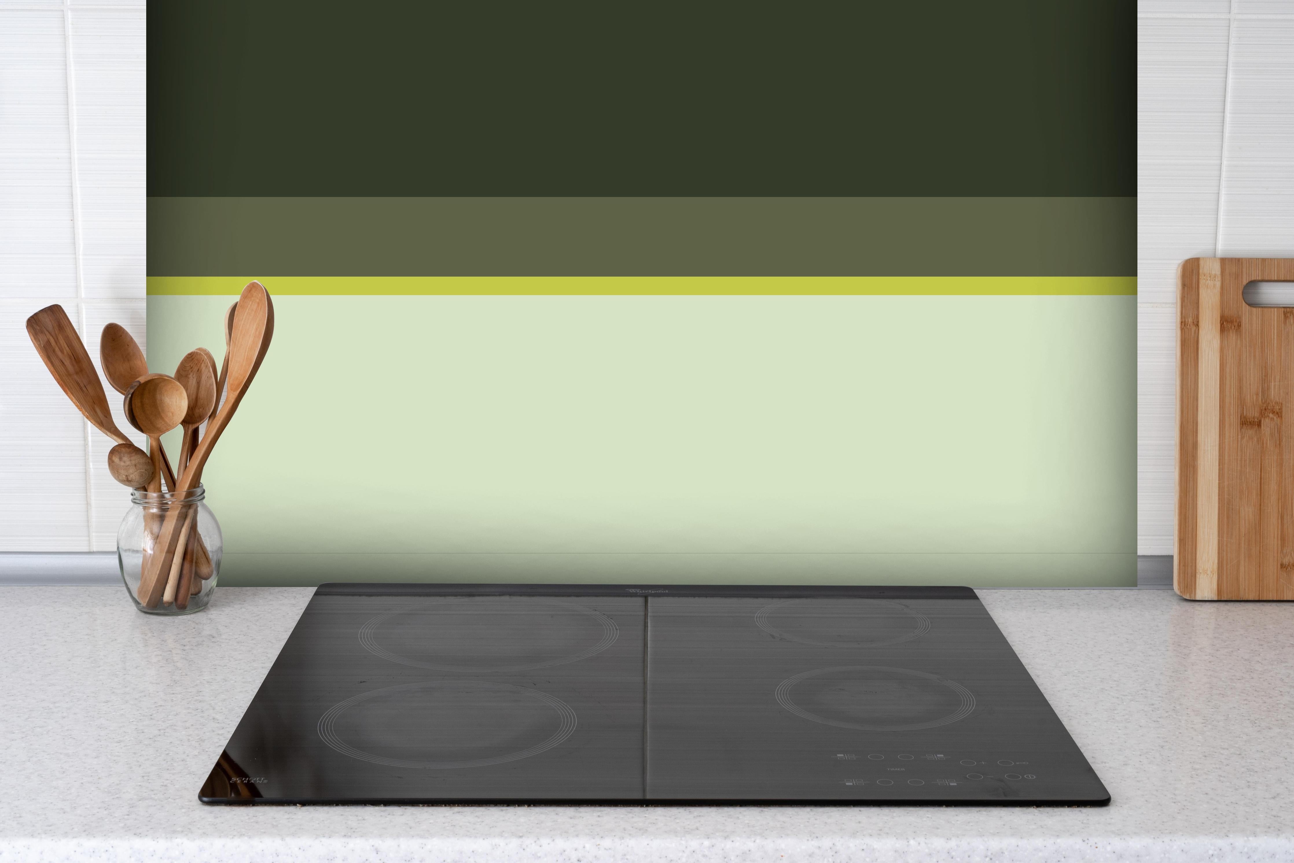 Spritzschutz - The Greens - Horizontal - Olive hinter einem Cerankochfeld zwischen Holz-Kochutensilien