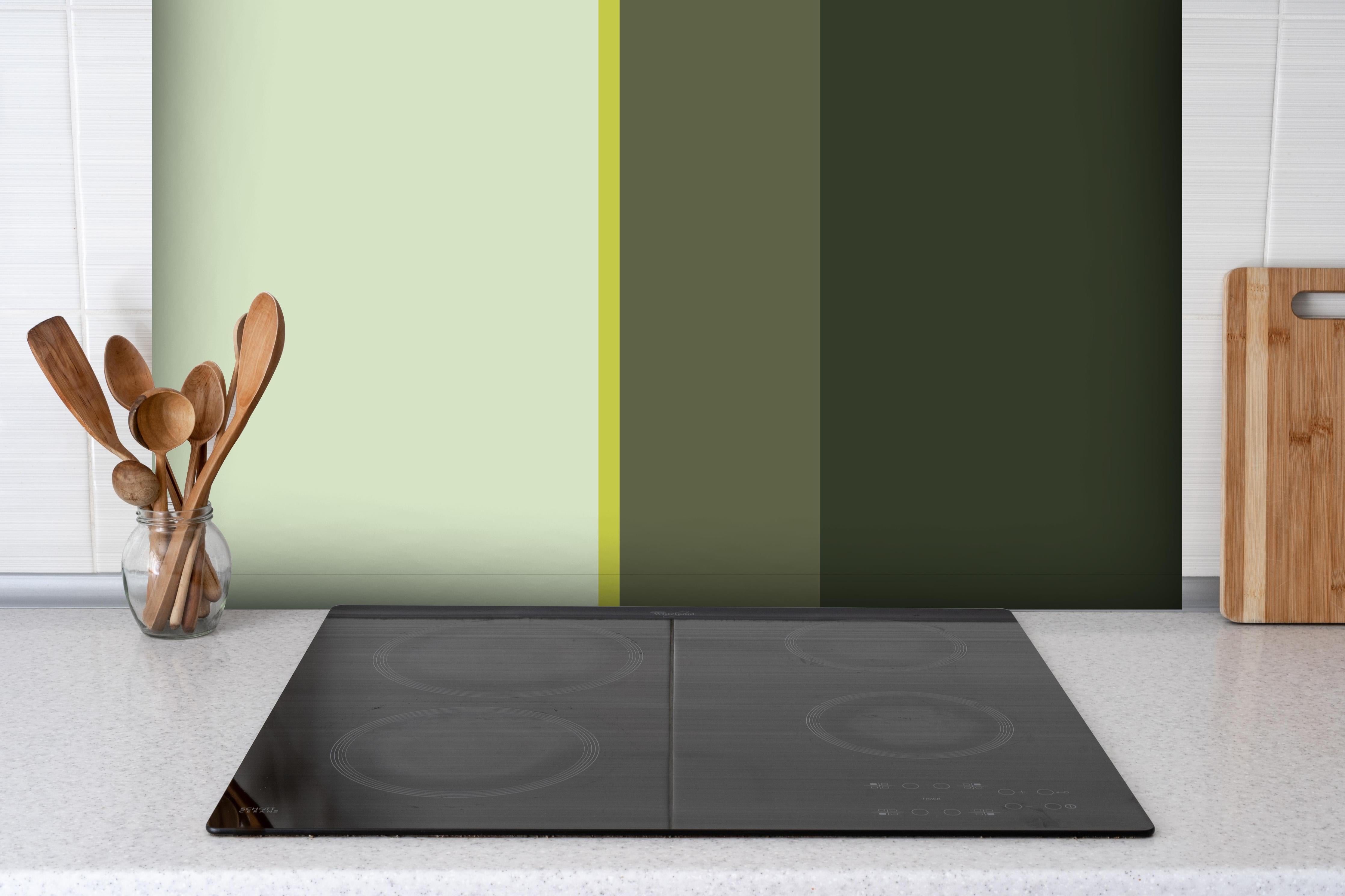 Spritzschutz - The Greens - Vertical - Olive hinter einem Cerankochfeld zwischen Holz-Kochutensilien