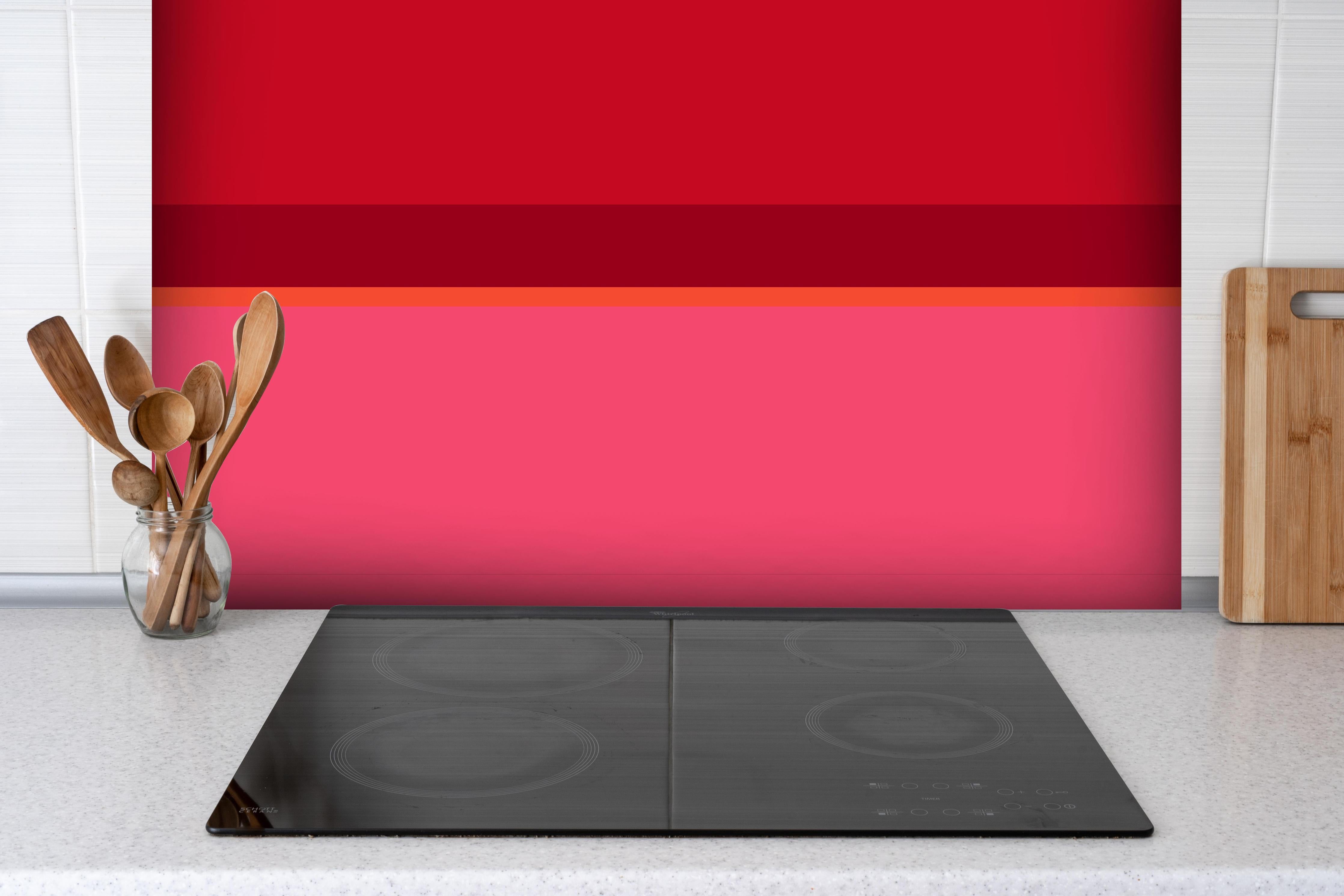 Spritzschutz - The Reds - Horizontal - Pommagranate hinter einem Cerankochfeld zwischen Holz-Kochutensilien