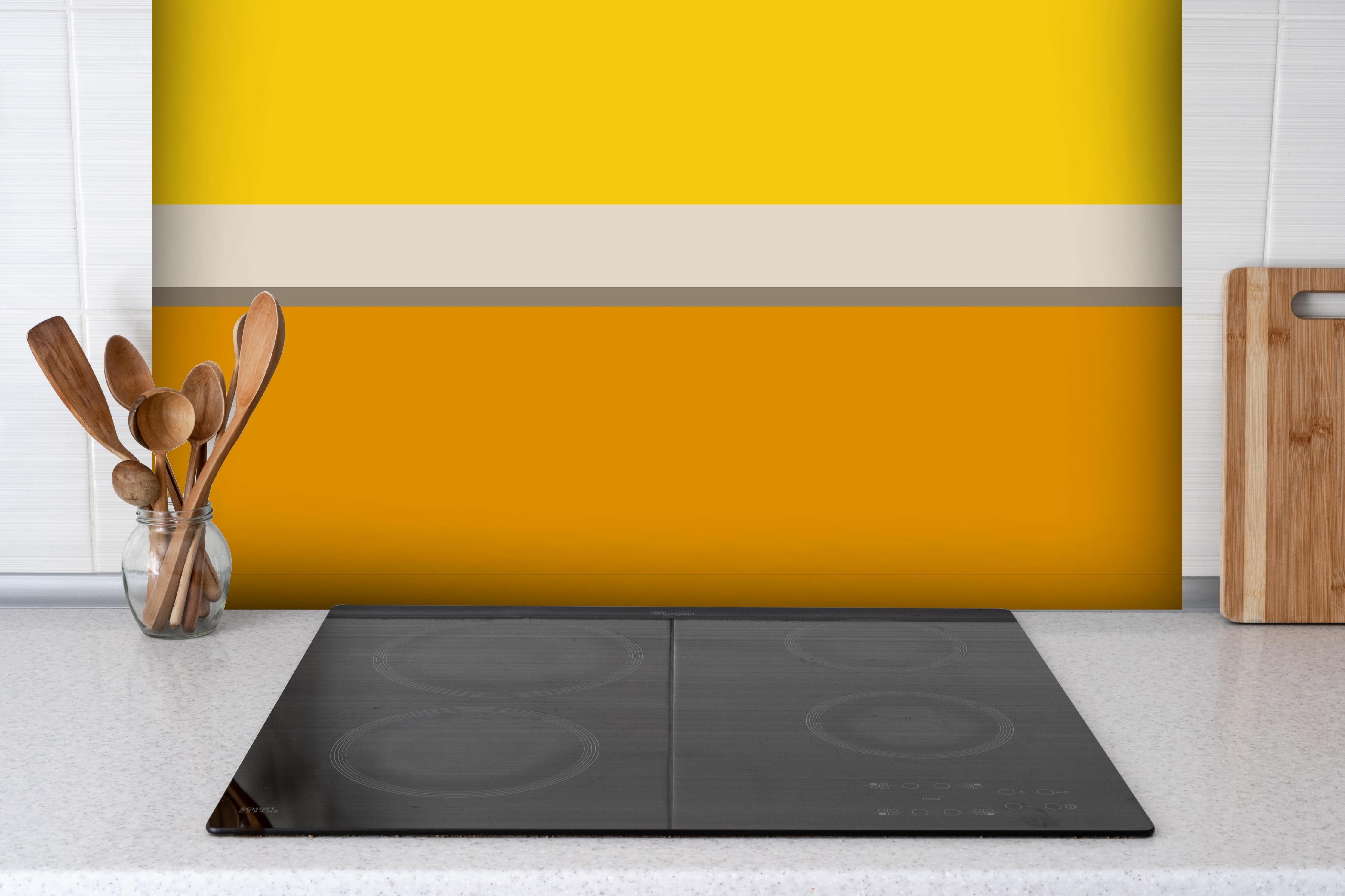 Spritzschutz - The Yellows - Horizontal - Saffron hinter einem Cerankochfeld zwischen Holz-Kochutensilien
