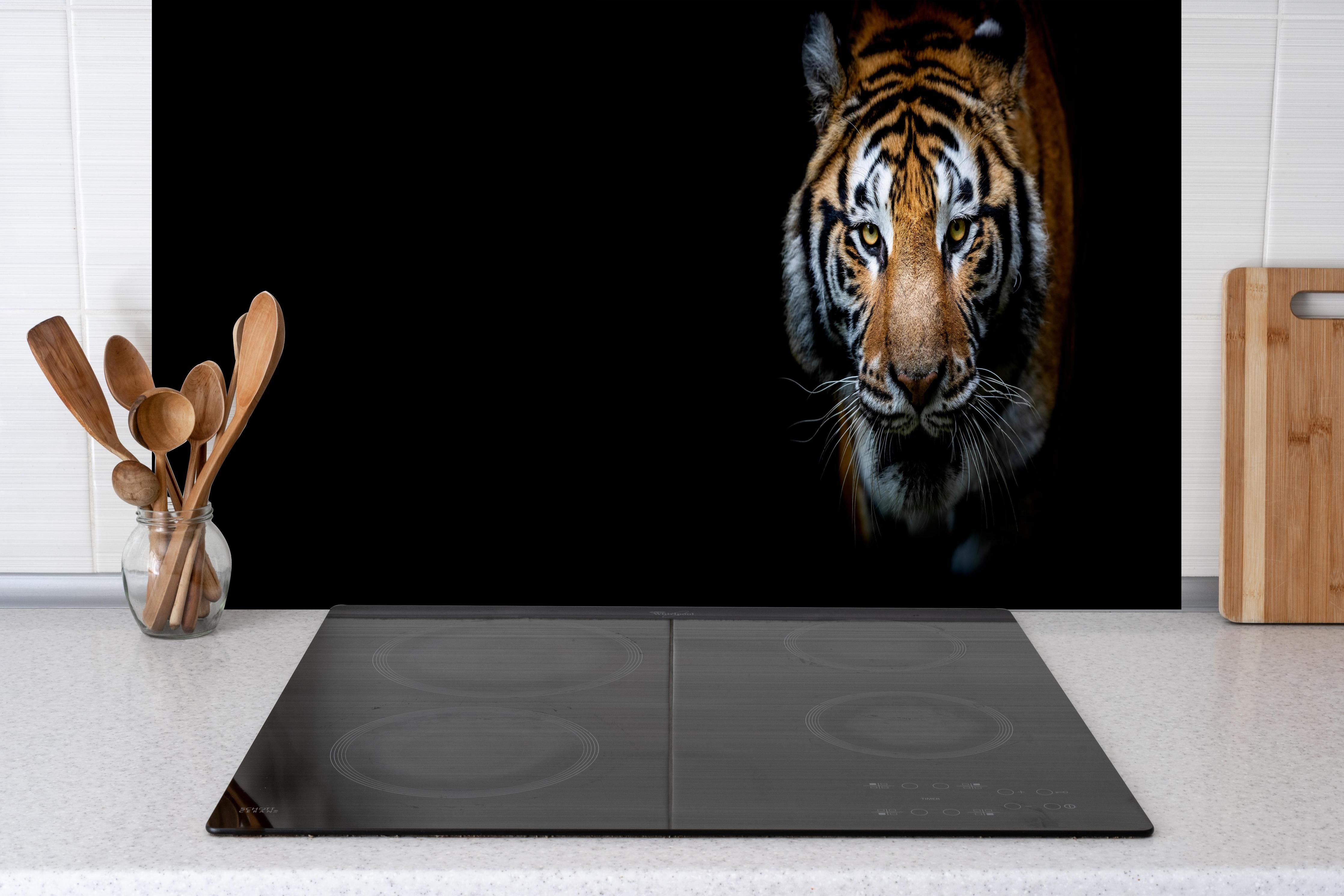 Spritzschutz - Tiger auf schwarzem Hintergrund hinter einem Cerankochfeld zwischen Holz-Kochutensilien