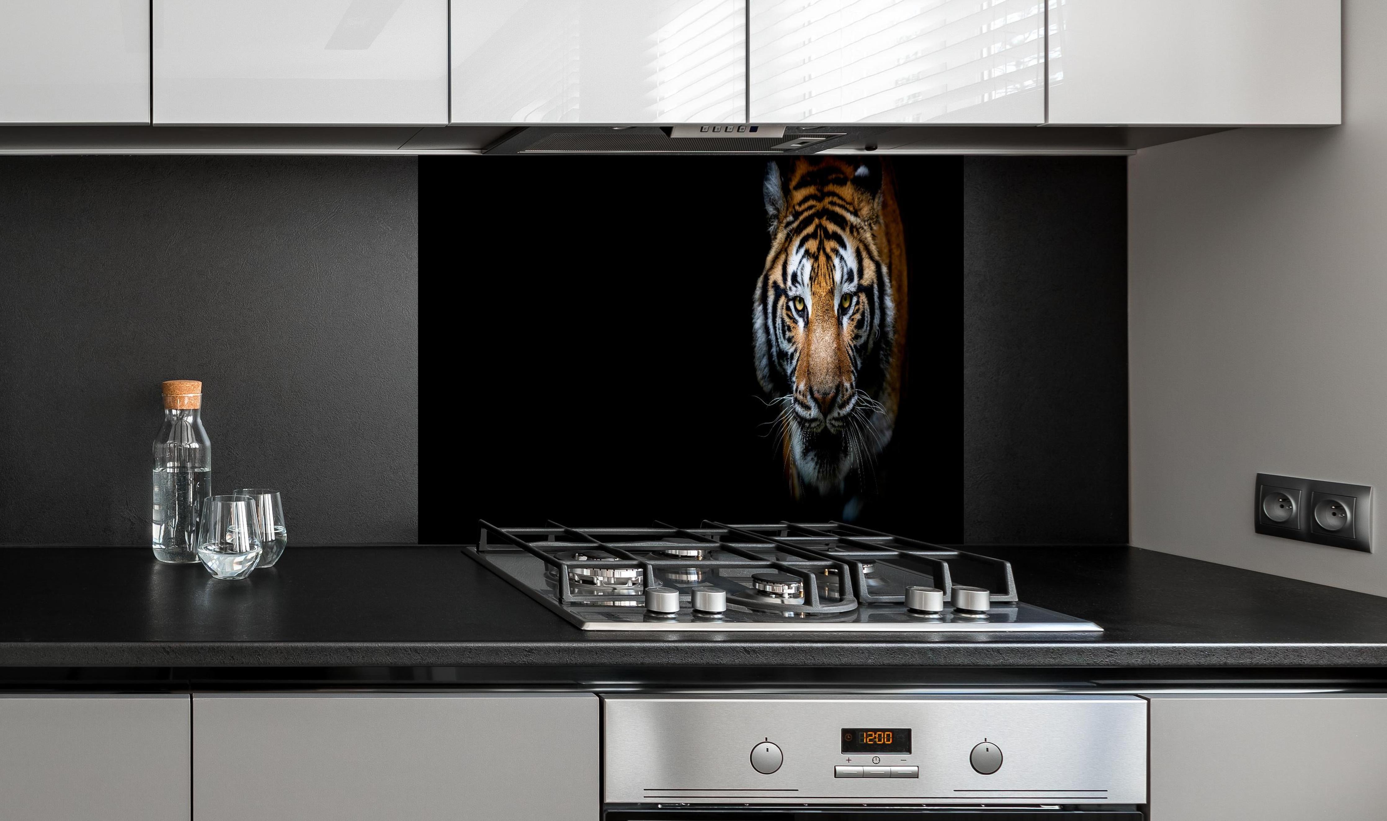 Spritzschutz - Tiger auf schwarzem Hintergrund hinter einem Cerankochfeld zwischen Holz-Kochutensilien