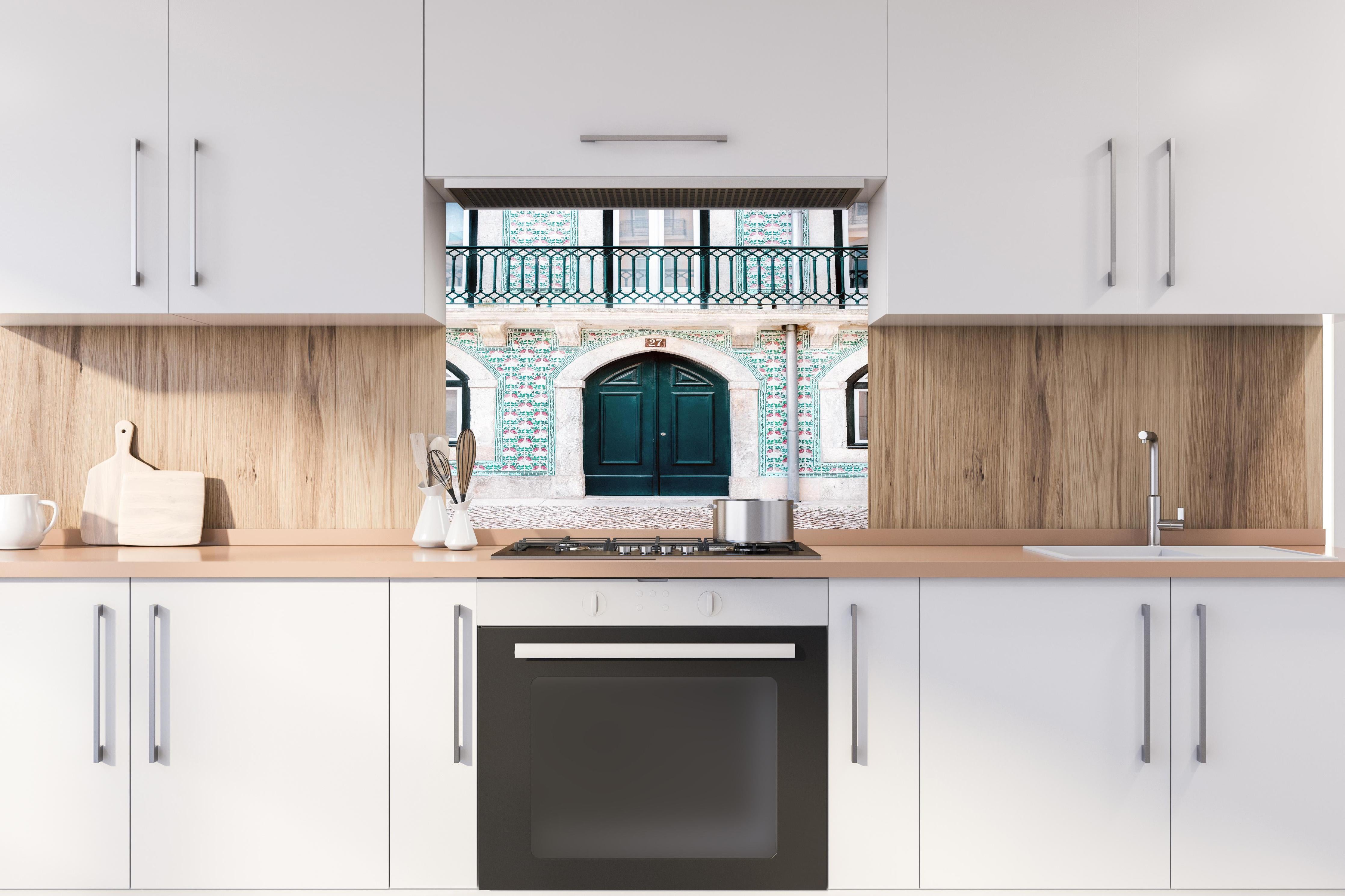 Spritzschutz - Traditionelle Tür Lissabons in Grün hinter einem Cerankochfeld zwischen Holz-Kochutensilien