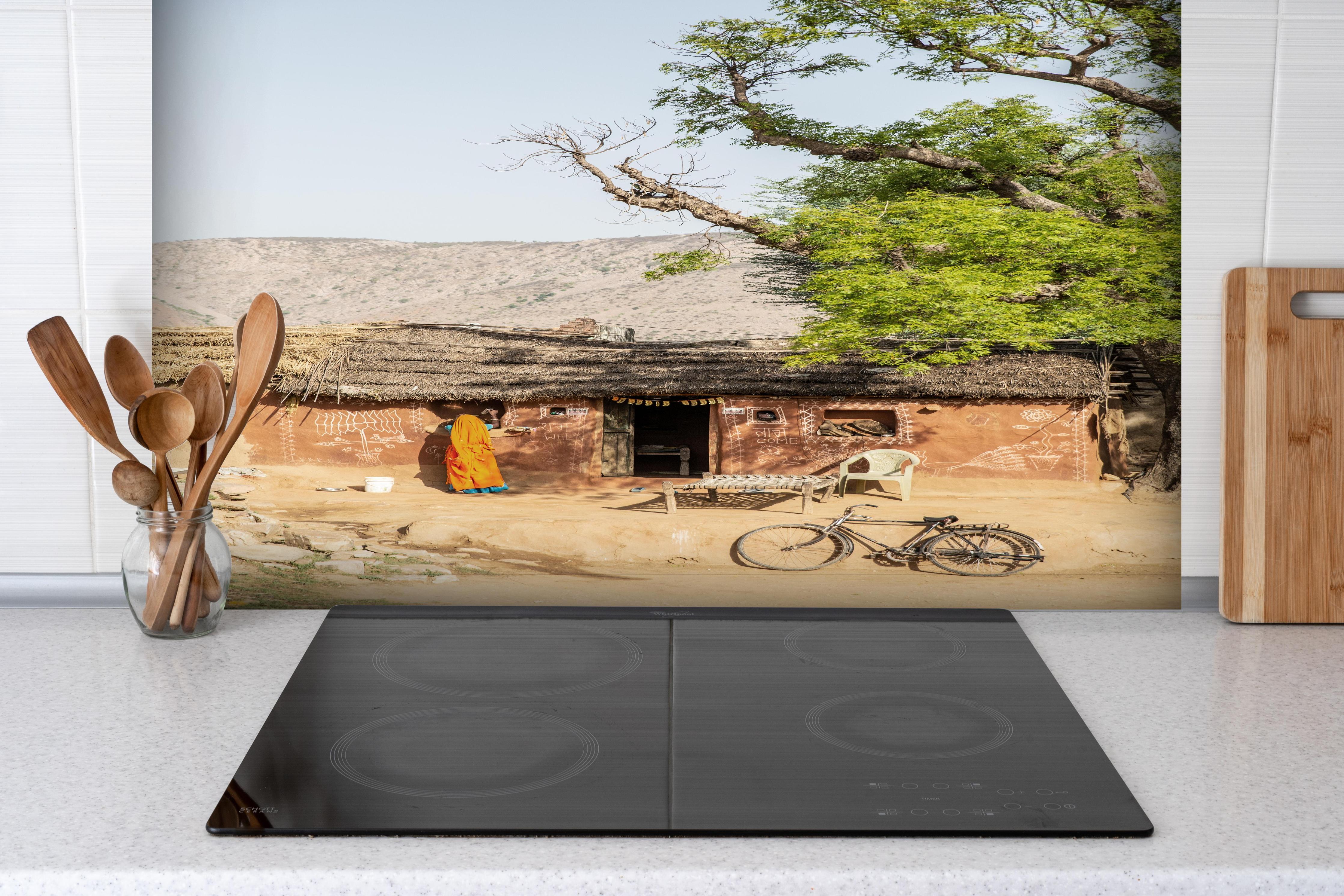 Spritzschutz - Traditionelles Dorf, Baum und Fahrrad hinter einem Cerankochfeld zwischen Holz-Kochutensilien