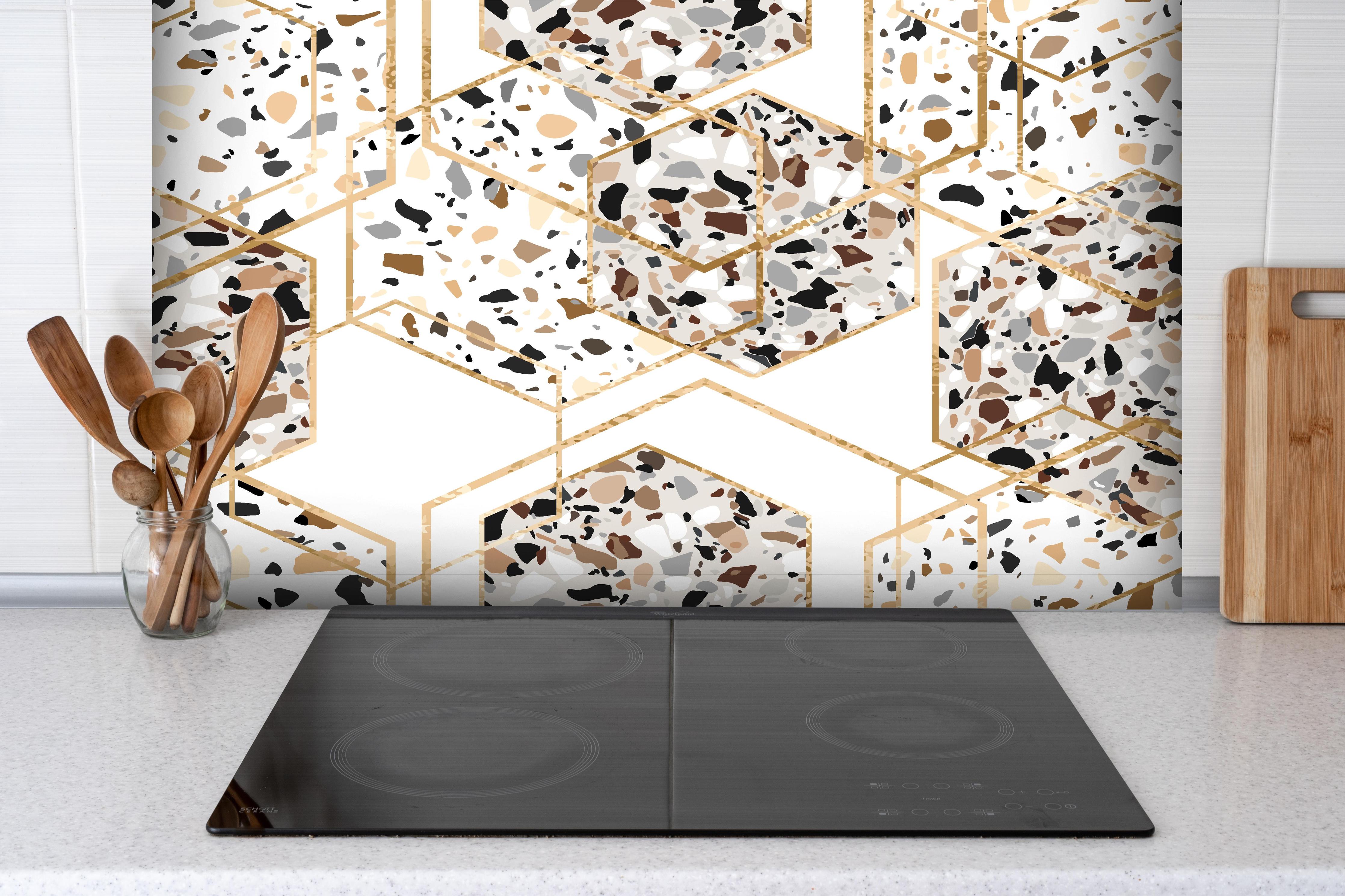 Spritzschutz - Trendiges Terrazzo-Muster mit Goldakzenten hinter einem Cerankochfeld zwischen Holz-Kochutensilien
